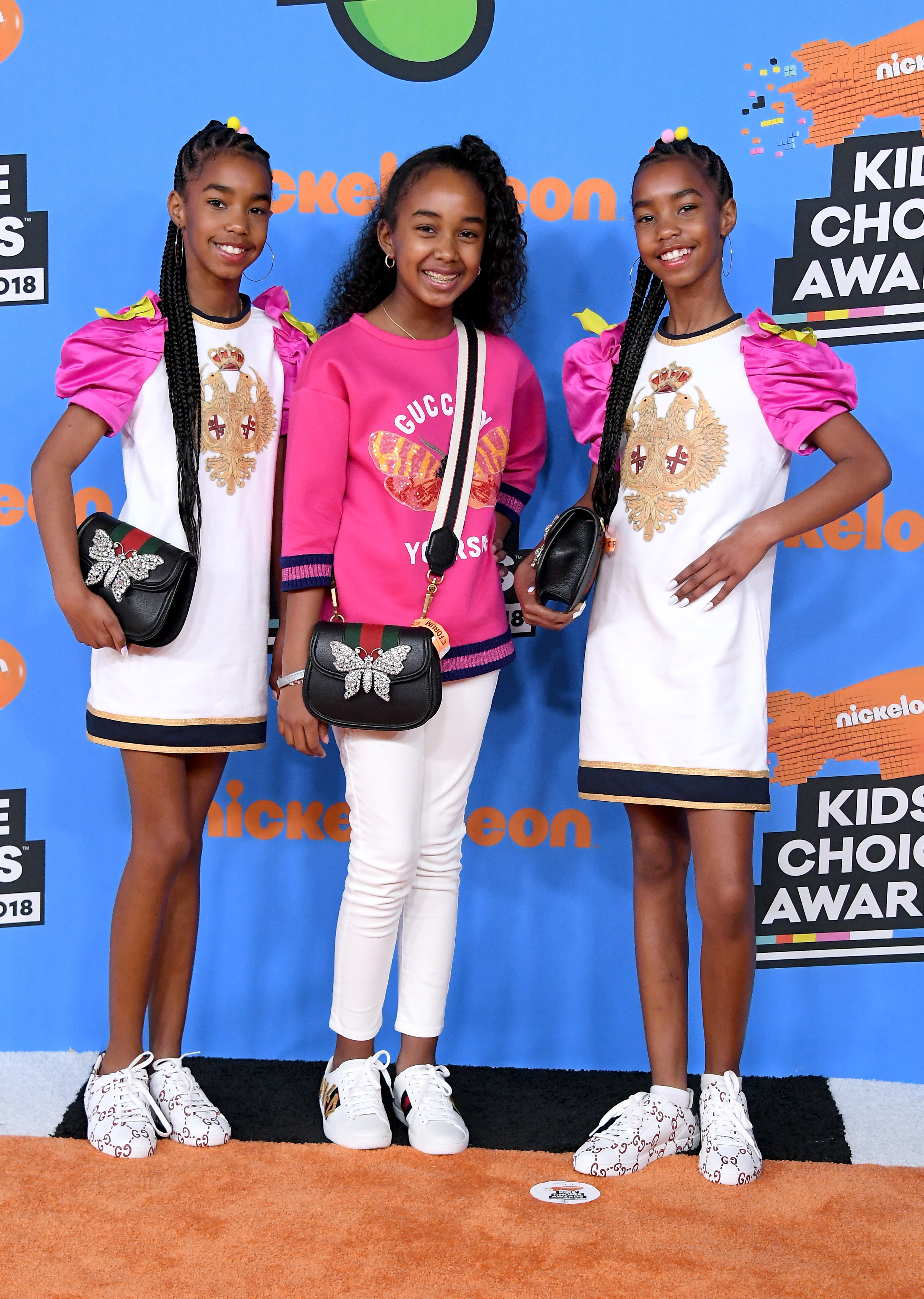 D'Lila, Chance and Jessie Combs s pose brightly on the orange carpet, dressed in bold colors, matching accessories, and playful designer details. Their confident smiles and coordinated outfits bring a fun, fashion-forward sparkle to the Kids’ Choice Awards backdrop.