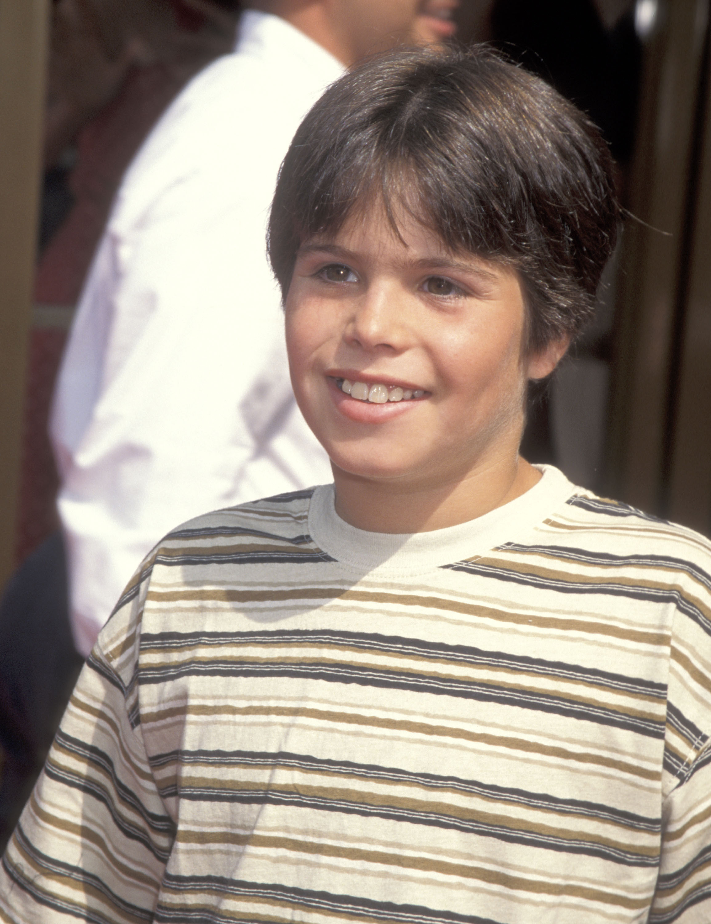 The young actor smiles in a striped T-shirt during a Hollywood appearance, looking noticeably older than the little boy audiences first fell in love with on screen.