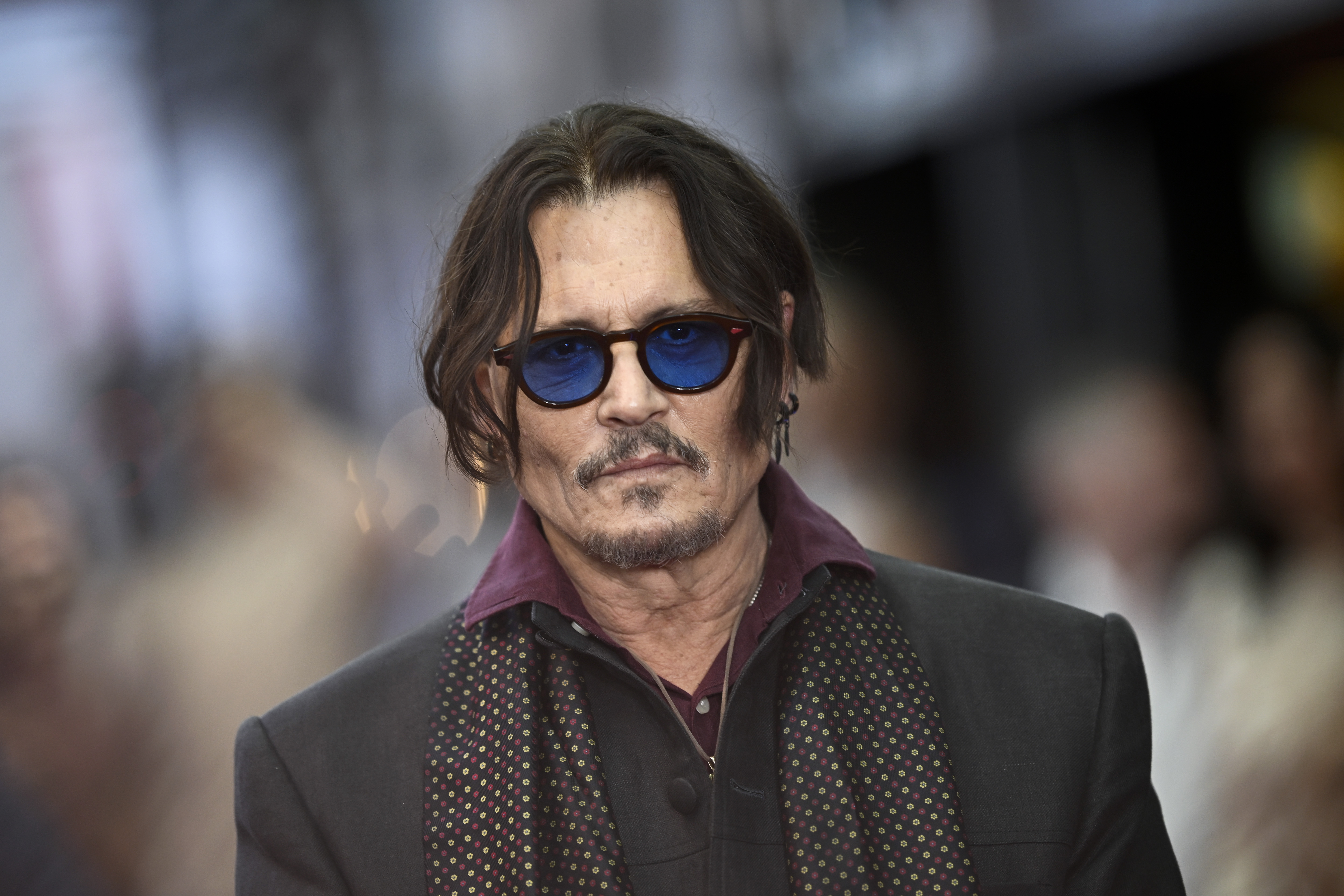 Johnny Depp poses for photos in blue-tinted sunglasses at the UK premiere of "Modigliani: Three Days on the Wing of Madness" in London on July 8, 2025 | Source: Getty Images