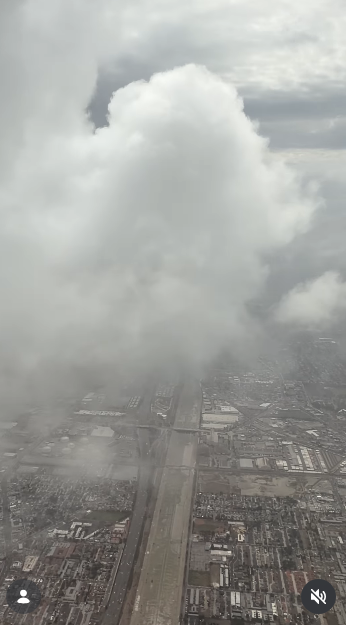 An airplane window perspective frames heavy overcast storm clouds hanging over expansive city grids and highways on October 11, 2026. Towering cumulus masses fill the sky, partially obscuring the urban layout below during transit. | Source: Instagram/selmablair