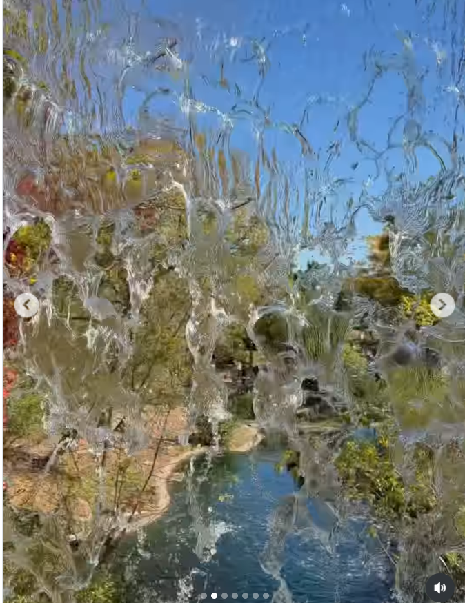 Sunlight glistens across a cascading water feature as trees with changing autumn foliage and a clear blue sky reflect in the moving water. | Source: Instagram/lindsaylohan