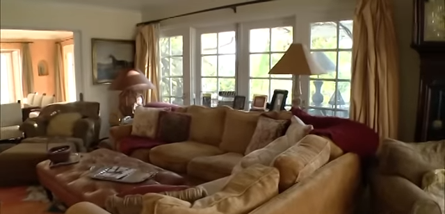 A massive neutral-toned sectional and an oversized tufted leather ottoman anchor the main seating space. | Source: YouTube/@Biography