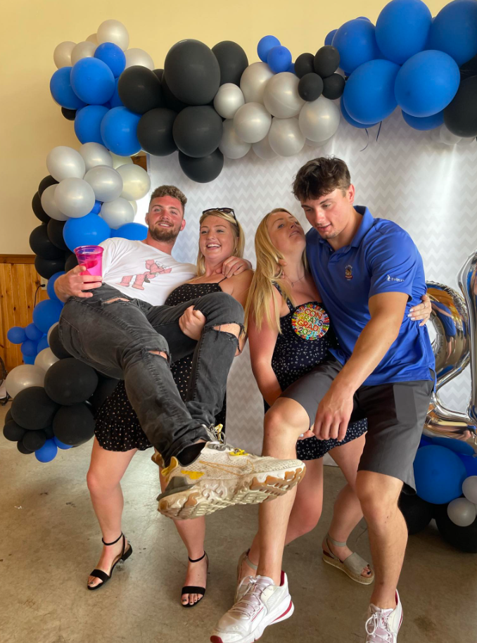 In front of a balloon backdrop, Jack Pugh helps hoist a friend mid-laugh — balance, effort, and celebration all colliding in one playful moment. | Source: Facebook/KennaLynMcClelland