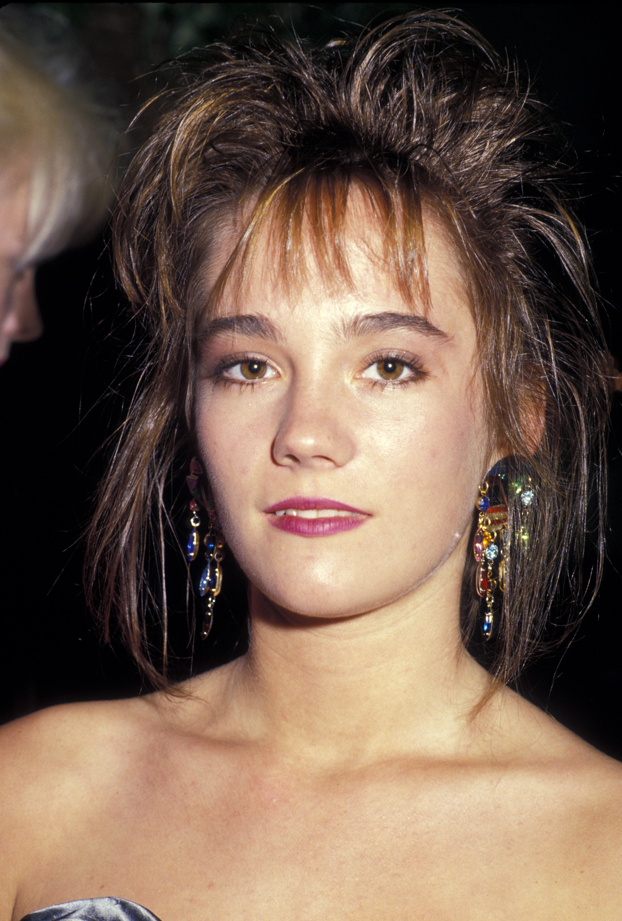 Natasha Gregson Wagner attends the 39th Annual Emmy Awards on September 20, 1987, at the Pasadena Civic Auditorium. She wears a strapless dress with colorful dangling earrings and her hair styled in a voluminous, tousled look.