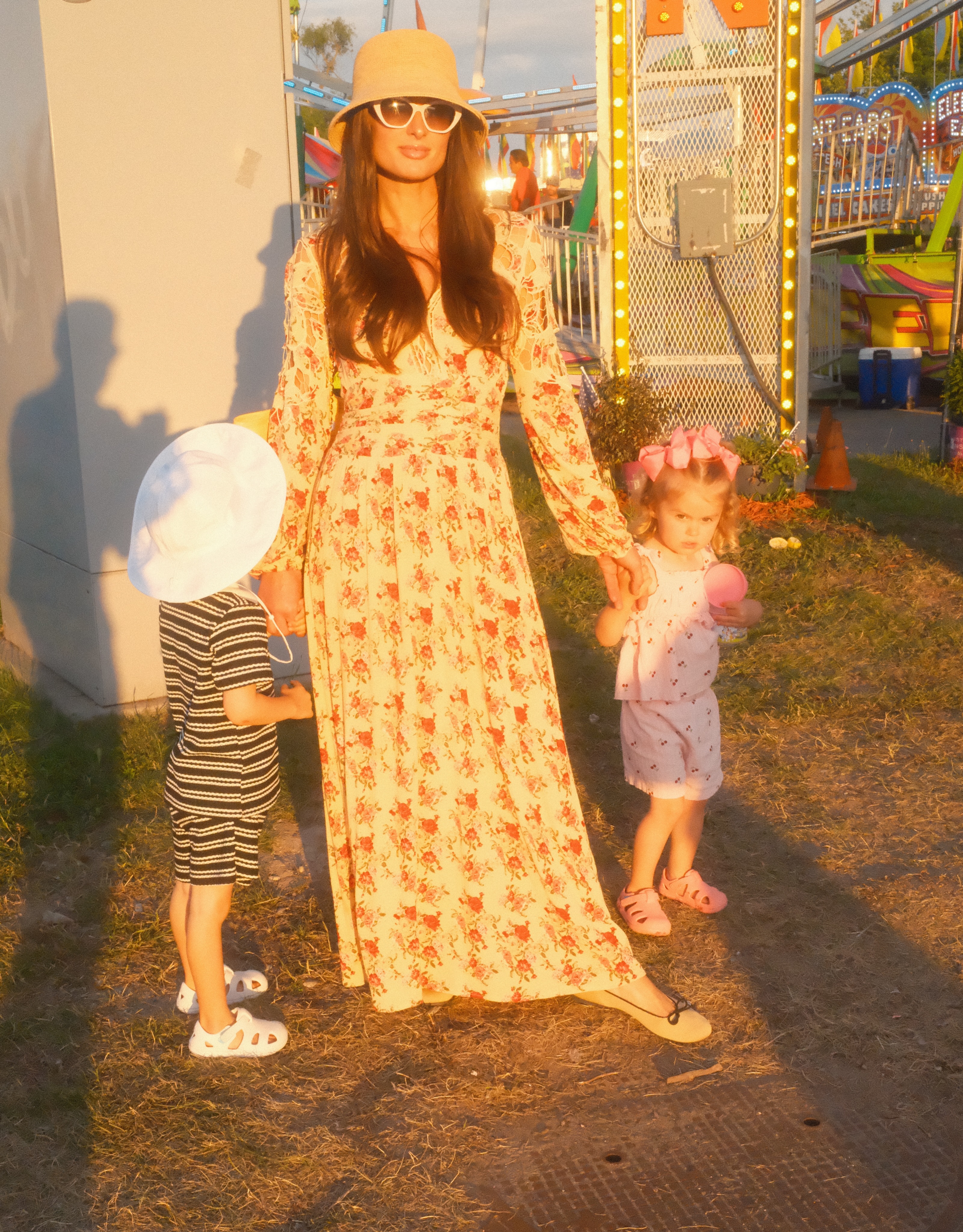 Paris's floral maxi dress, bucket hat, and sunglasses helped create the relaxed look that drew so much attention online. Her long brunette hair made the ensemble feel especially different from her familiar platinum-blonde image. | Source: Instagram/parishilton