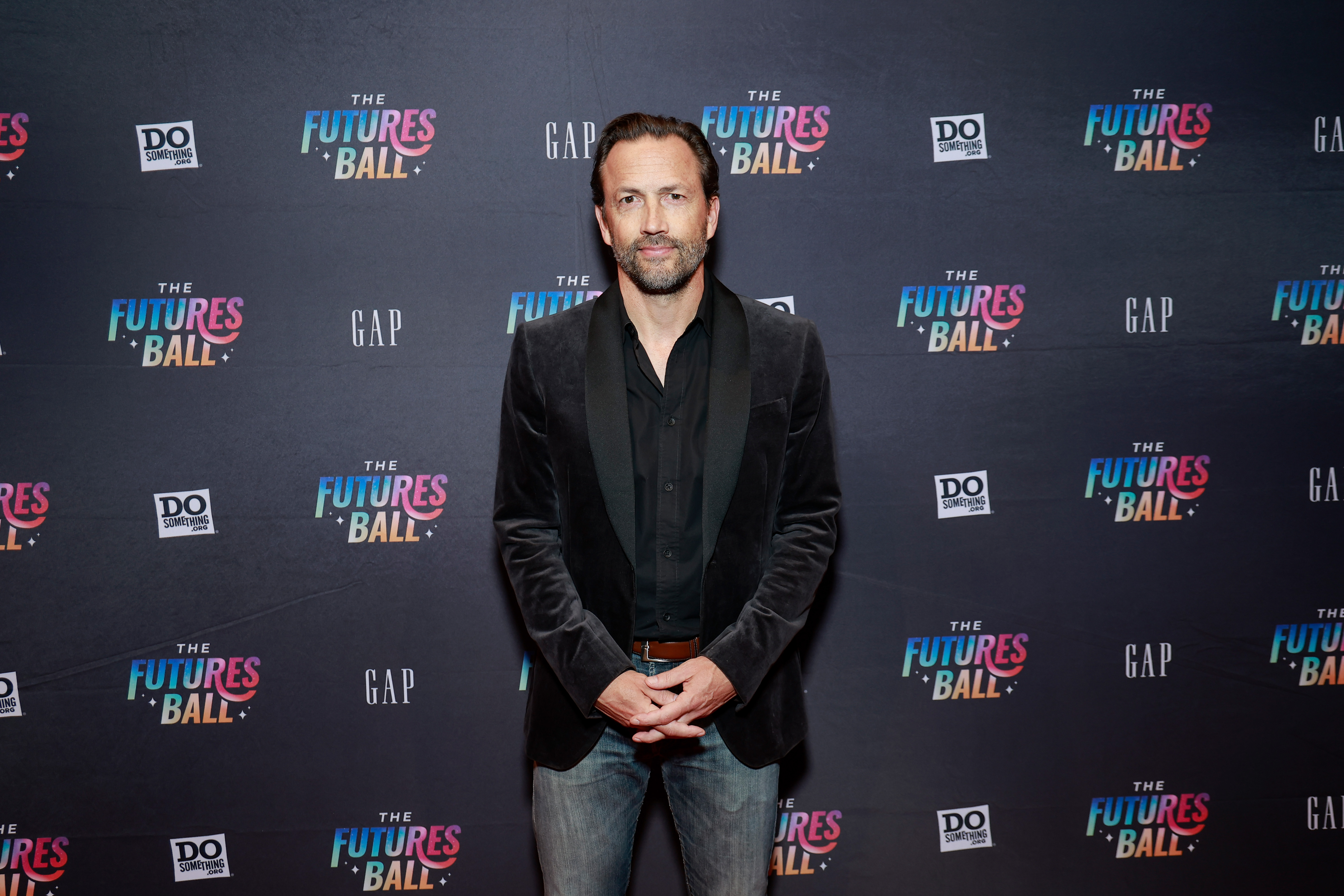 Andrew Shue stands for portraits on the red carpet at Do Something's The Futures Ball 30th Anniversary Celebration at The Ziegfeld Ballroom in New York City on November 16, 2023. The "Melrose Place" star opts for smart-casual evening styling, wearing a black velvet jacket over an unbuttoned dark shirt, faded denim jeans, and a brown leather belt. | Source: Getty Images