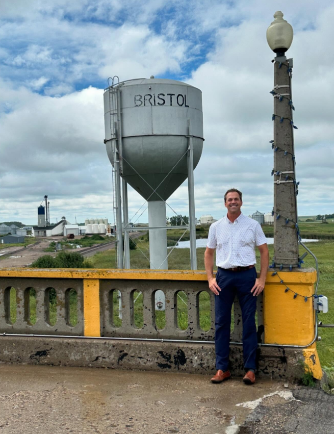 Bryon Noem stands by a bridge with the “Bristol” water tower behind him—small-town skyline, open fields, and a quiet sense of place. | Source: Instagram/sdbryonnoem