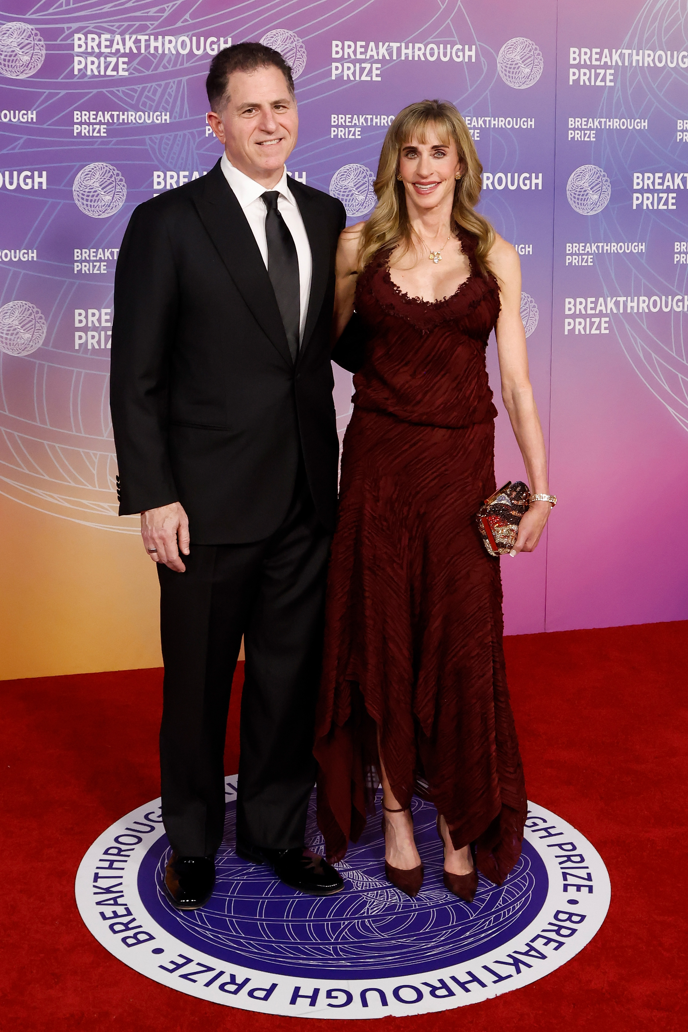 Susan Dell and her husband Michael Dell attend the 12th Breakthrough Prize Ceremony at Barker Hangar in Santa Monica, California. Susan wore a flowing burgundy gown with delicate detailing as the couple posed together on the red carpet.