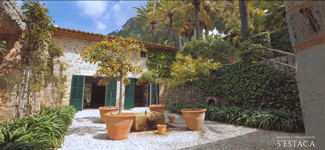 Potted citrus trees fill this peaceful courtyard, surrounded by stone walls, green shutters, ivy, and tall palms. The space shows how gardens and greenery are tucked between the estate's buildings. | Source: YouTube/billionsluxuryportal