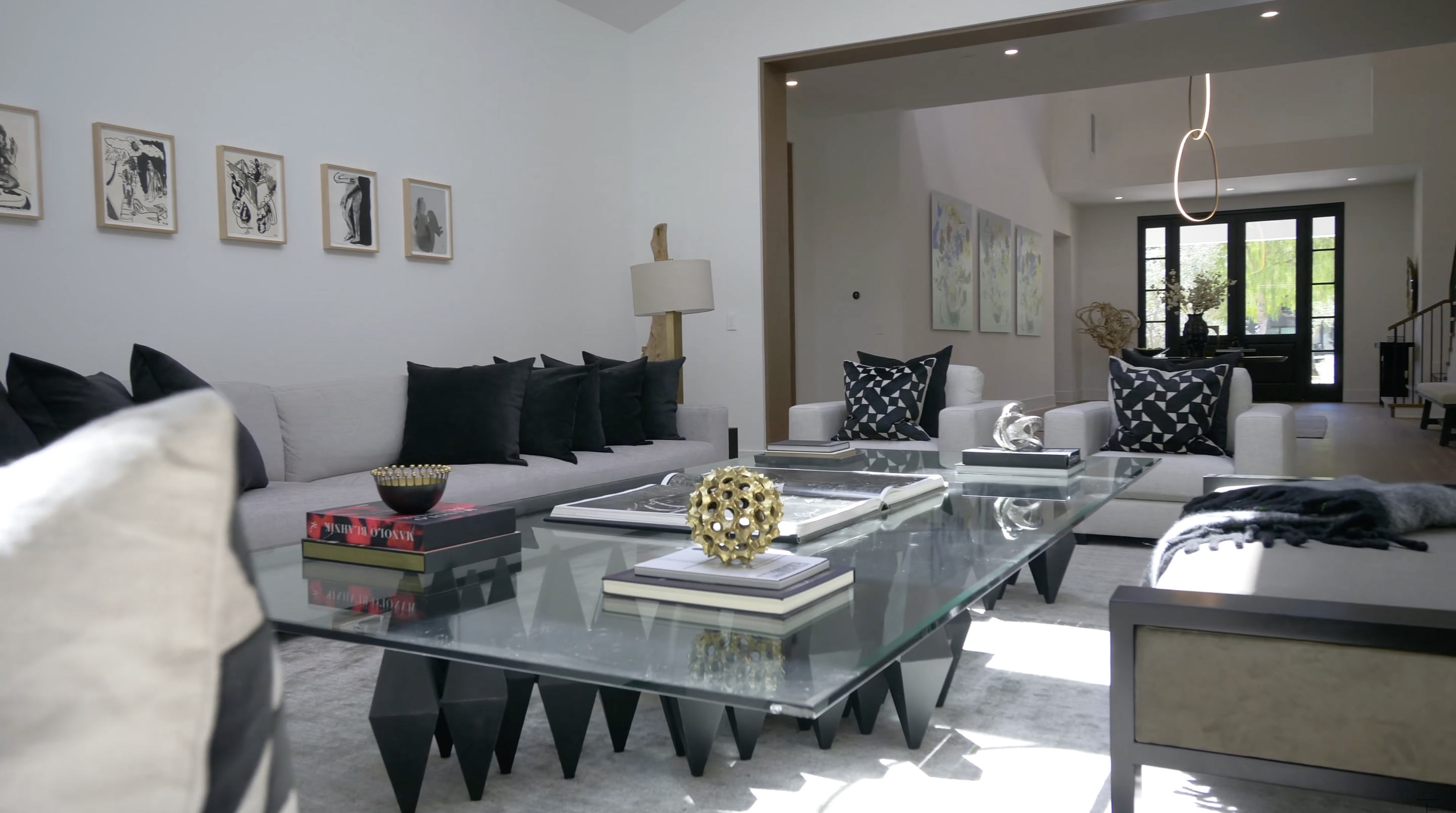 Pale sofas and armchairs are paired with dark pillows and a sculptural coffee table in this formal gathering space. A wide opening provides a direct sightline back toward the foyer. | Source: Youtube/Tomer.Fridman