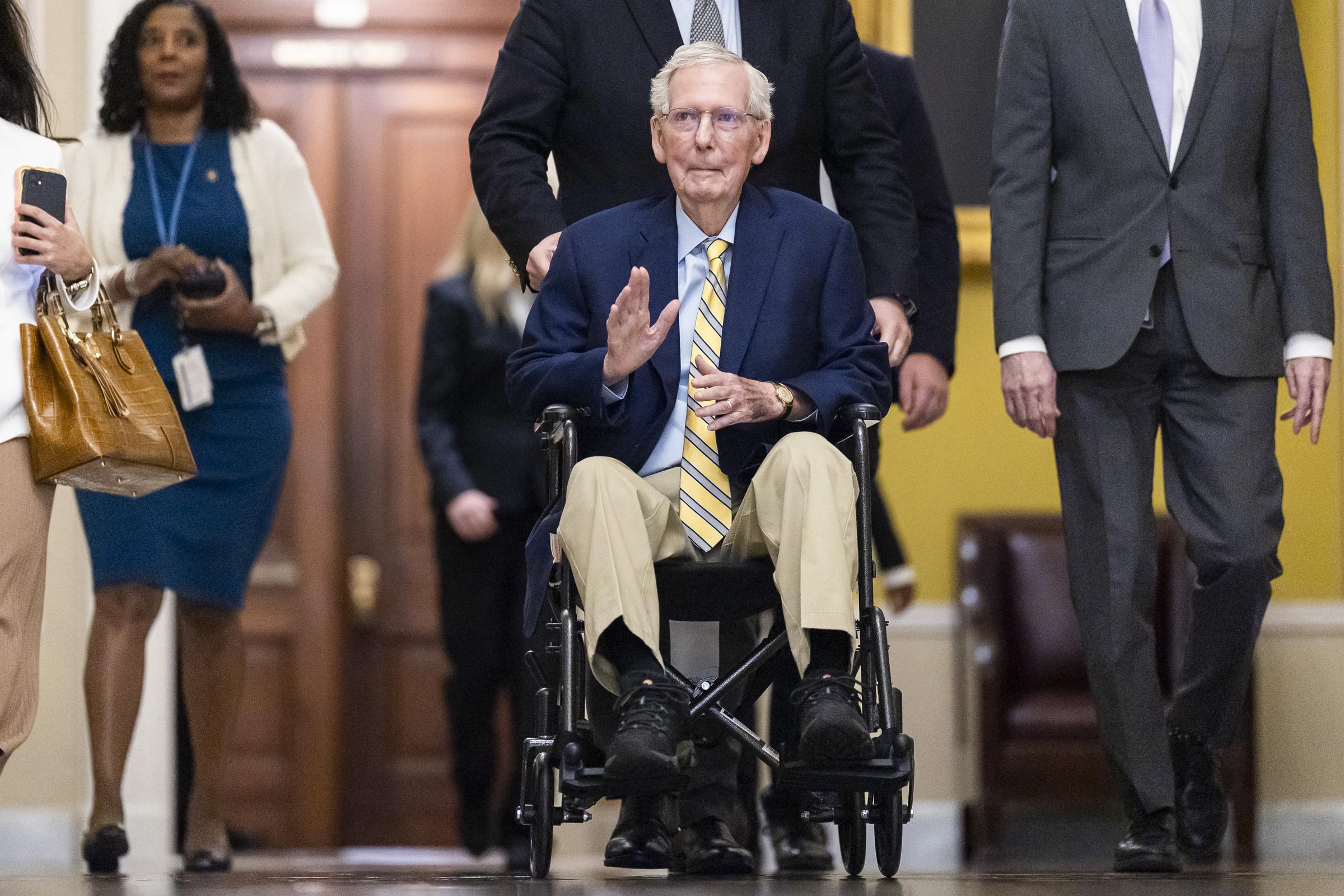 McConnell raises one hand while traveling through the U.S. Capitol in a wheelchair on September 14, 2026. His black shoes and the position of his feet are visible in the full-length view. | Source: Getty Images