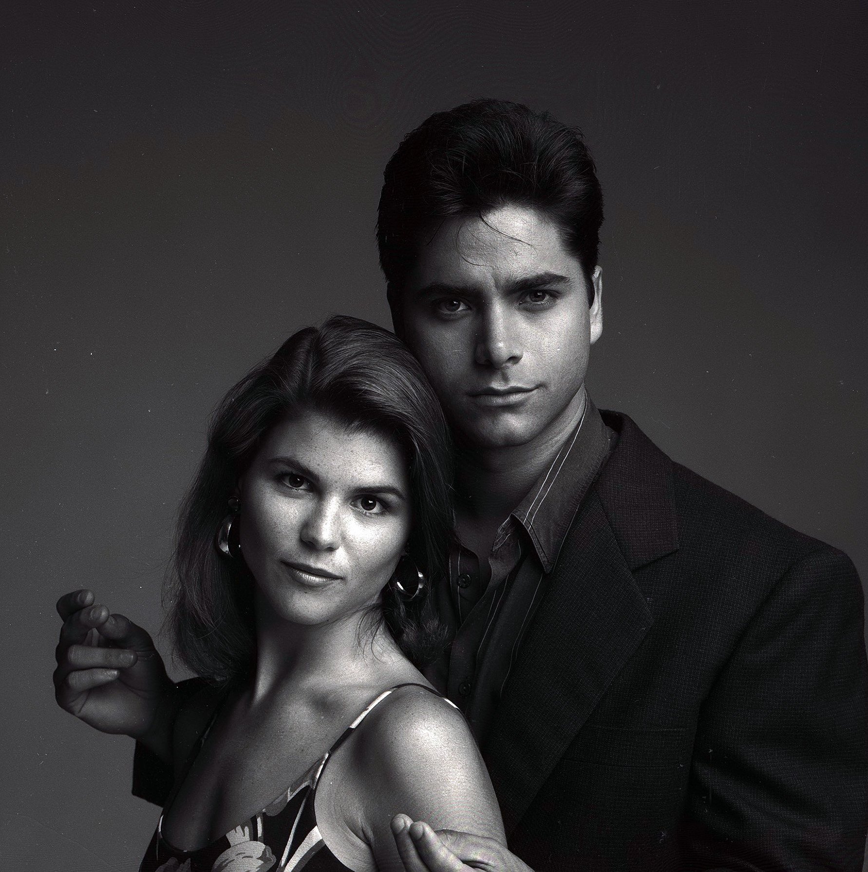 Lori Loughlin and John Stamos pose close together for a moody, black-and-white "Full House" cast gallery shoot on August 8, 1989. Capturing the effortless chemistry between Aunt Becky and Uncle Jesse, the portrait highlights the magnetic pairing that quickly became one of television's favorite couples. Loughlin leans gently against Stamos as he sports his trademark feathered hair and sharp blazer, reflecting the early charm of a screen romance that anchored so much of the beloved series.