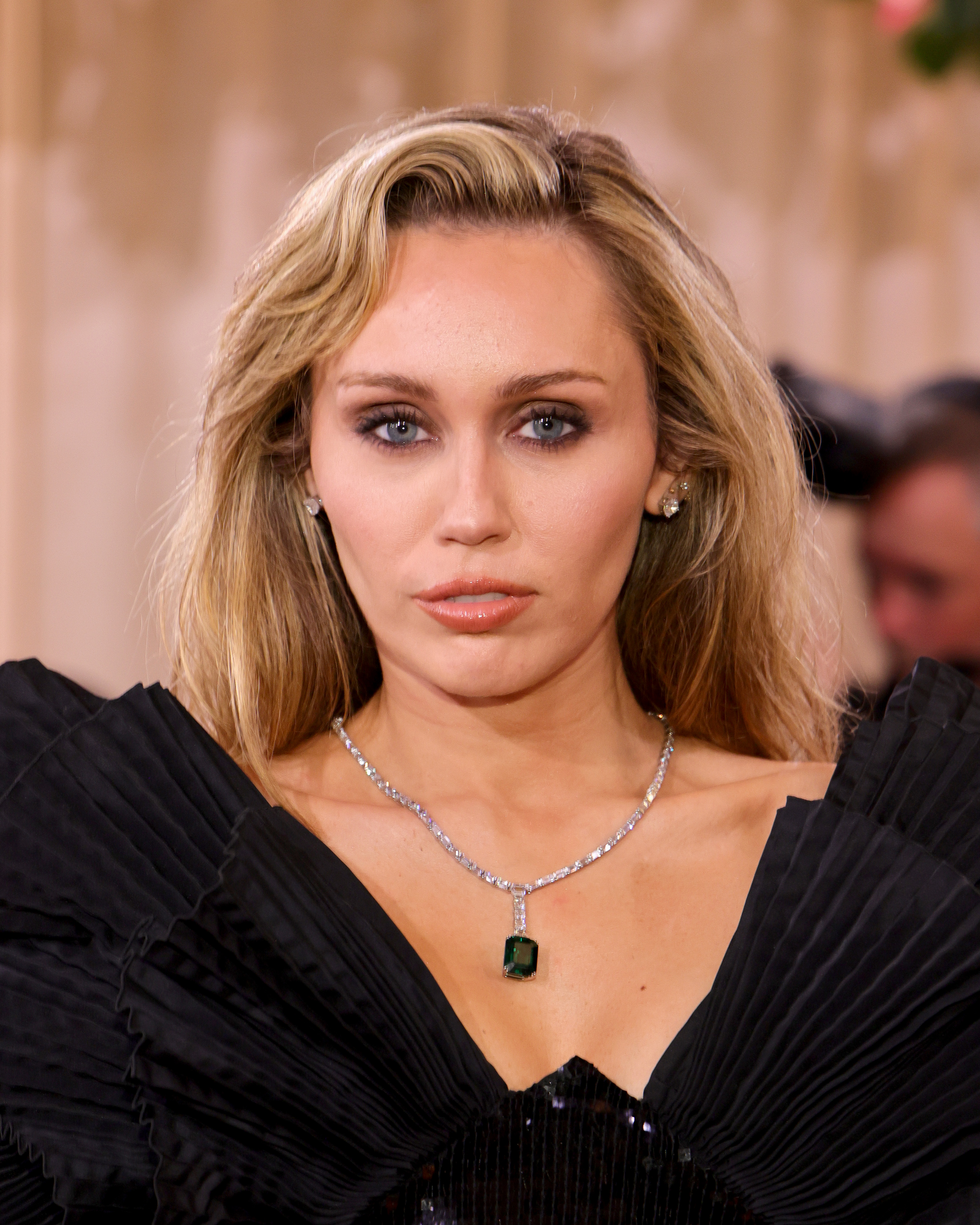 Miley Cyrus posed in a black gown with dramatic pleated shoulders and a statement emerald necklace. Her smile adds another frame to the visual comparisons explored by Lange and Linkov, but differences in how the teeth and gums appear across photographs do not prove that she underwent a gum lift, received veneers, or had Botox injections. | Source: Getty Images