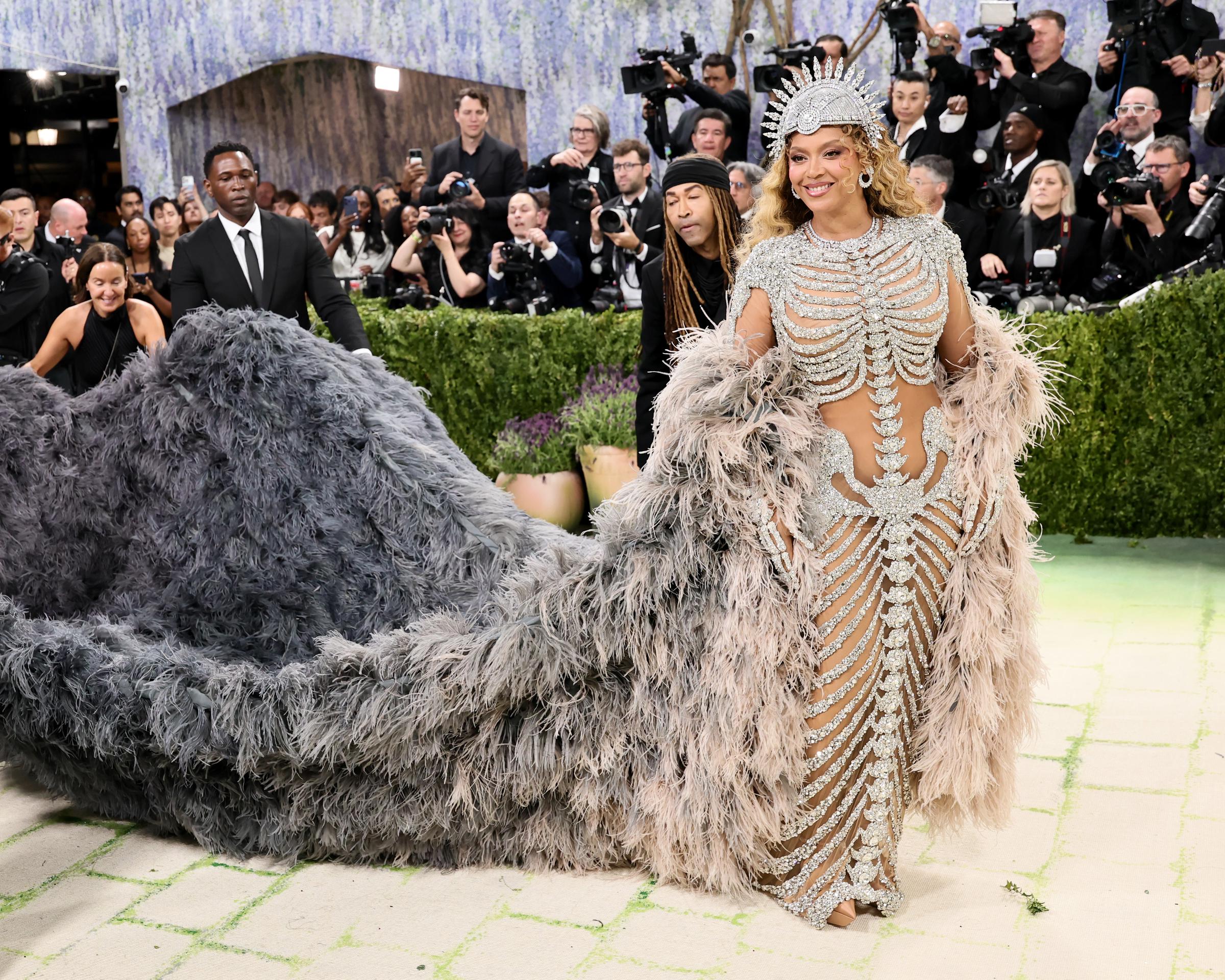 Beyoncé smiles as attendants help arrange the long train of her coat | Source: Getty Images