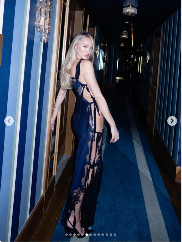 Candice Swanepoel turns heads in a navy-blue evening gown with sheer lace panels and delicate cutout details, posing in a stylish corridor. The striking look offers another glimpse of the supermodel's glamorous life beyond the runway. | Source: Instagram/candiceswanepoel