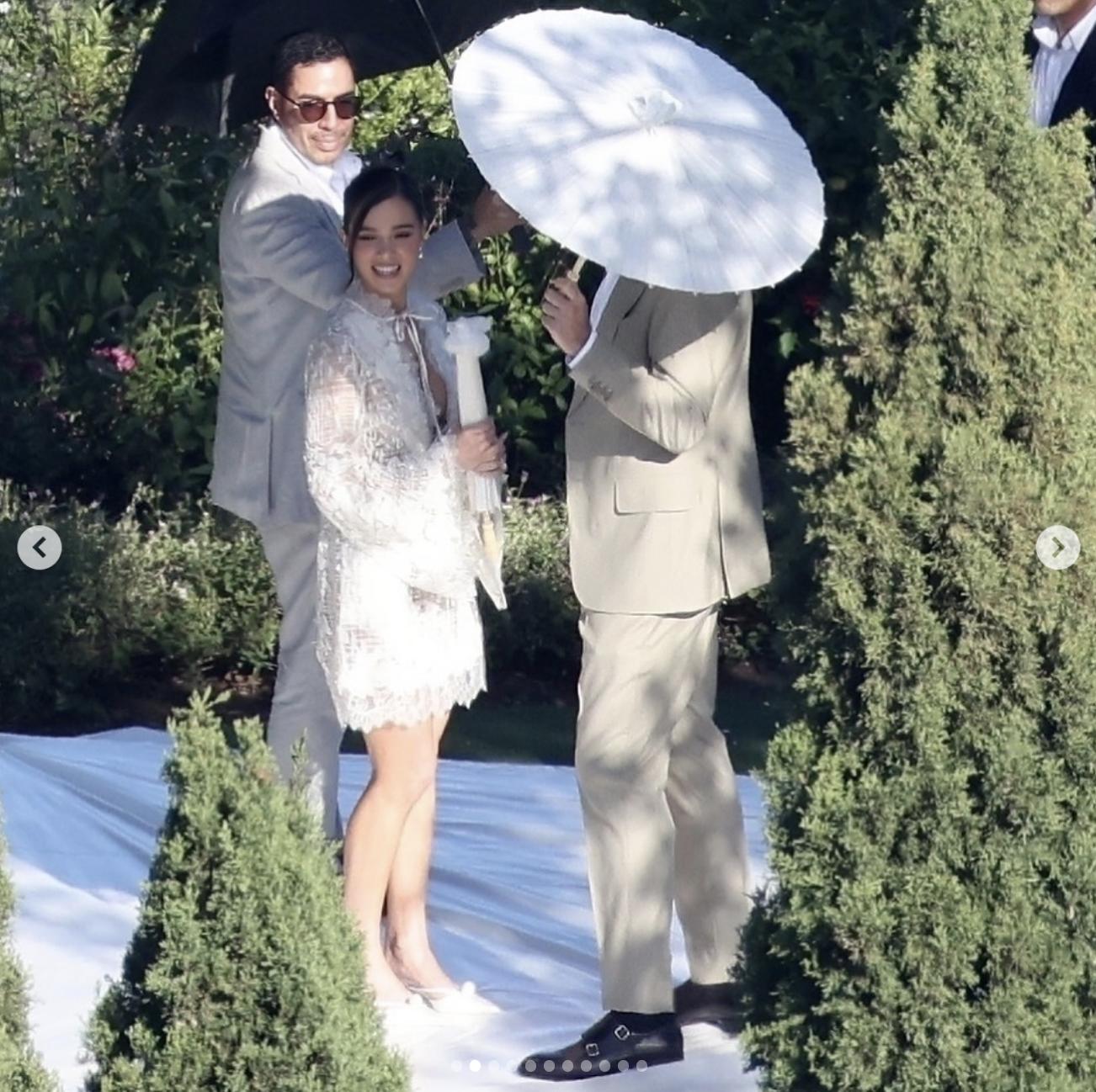 Hailee Steinfeld smiles during the walk-through, holding a white parasol as the team looks on | Source: Instagram/deuxmoi