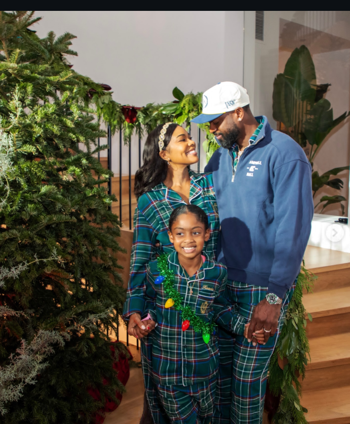 In a festive indoor setting, Gabrielle Union and Dwyane Wade stand close together beside a decorated Christmas tree with their daughter in front. | Source: Instagram/gabunion