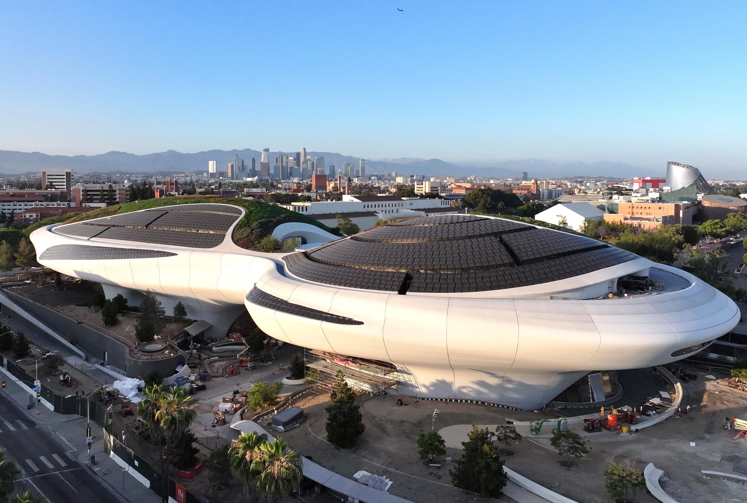 An aerial view shows the Lucas Museum of Narrative Art's sweeping form and expansive rooftop as the building neared completion. The surrounding Los Angeles skyline provides a sense of the museum's scale within Exposition Park. | Source: Getty Images
