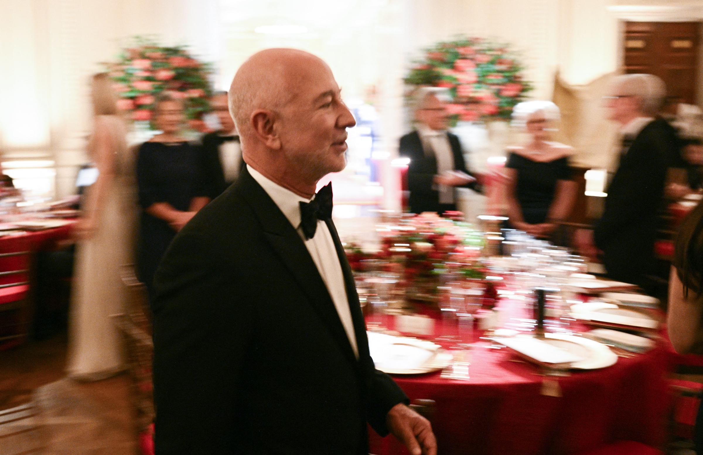 Jeff Bezos navigated the bustling East Room of the White House in a classic black tuxedo and bow tie during the state dinner honoring Chinese President Xi Jinping on September 24, 2026, in Washington, DC. Captured in a dynamic candid shot moving past banquet tables set with vibrant red linens and floral centerpieces, the Amazon founder joined fellow prominent business executives and dignitaries gathering for the evening's diplomatic festivities. | Source: Getty Images