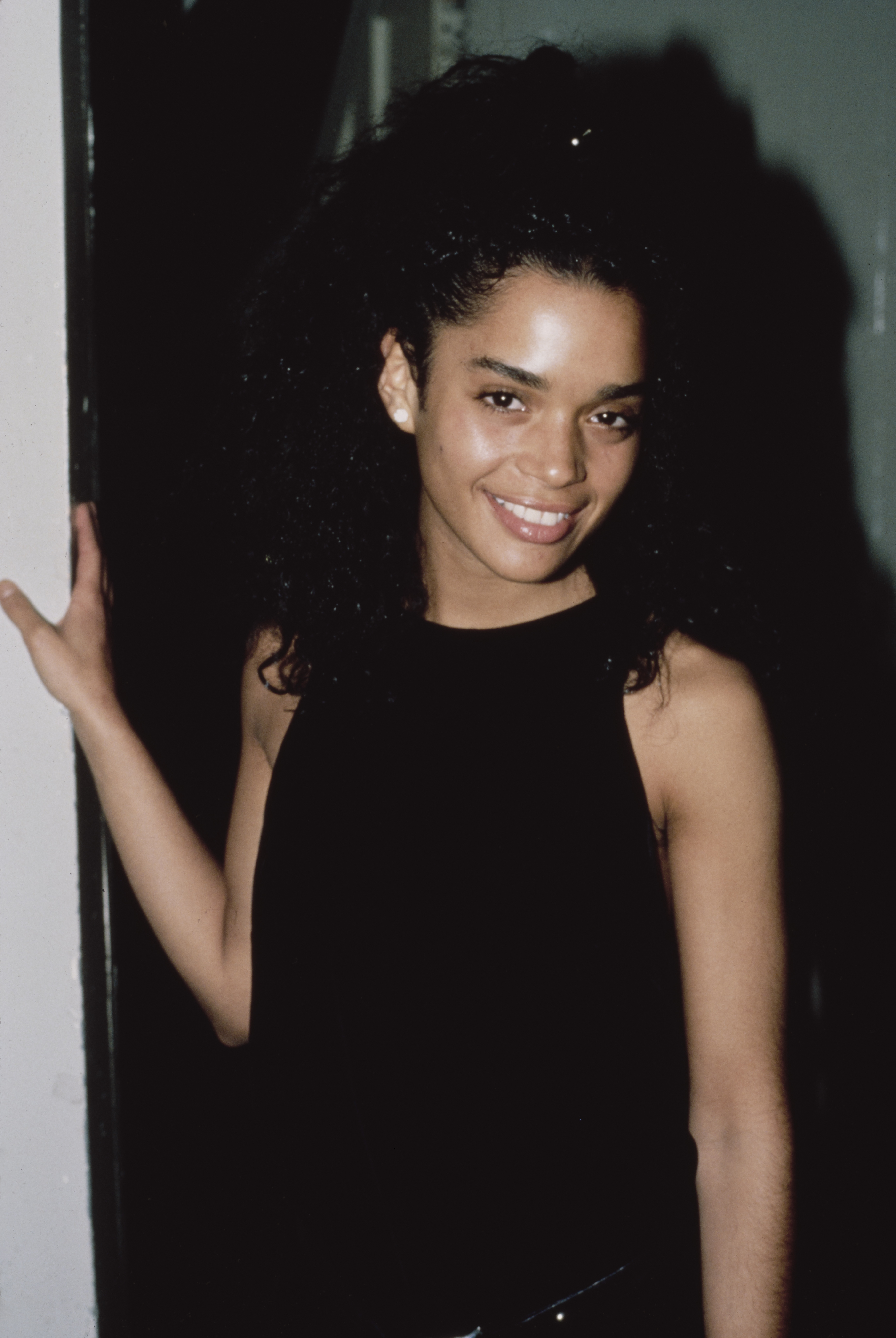 Lisa Bonet poses in a sleeveless black top with her hand resting on a doorway, showing the effortless charm that helped define her early Hollywood image.