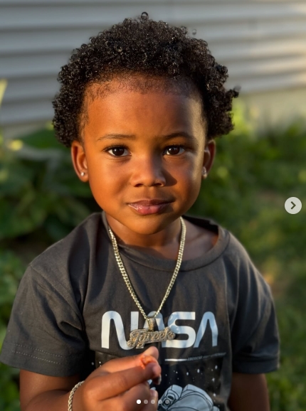 Now three years old, Tyreek Jr. looks into the camera during an outdoor portrait, showing off his curly hair while wearing a dark NASA T-shirt, stud earrings, a bracelet, and a chain bearing a "Tyreek" pendant. The August 1, 2026, post offered a recent glimpse of Tyreek Hill and Camille Valmon's growing son. | Source: Instagram/tyreekhilljr_