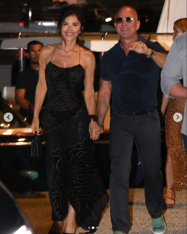 Lauren Sanchez and Jeff Bezos hold hands and smile as Bezos holds out his arm towards the camera while they walk through a Saint-Tropez restaurant, from a post dated July 23, 2025. | Source: Instagram/PageSix