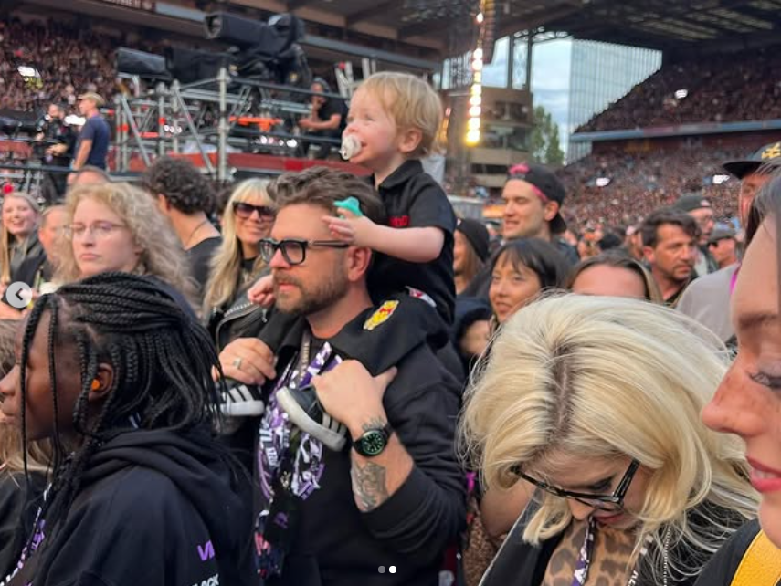 Jack Osbourne and one of his children is seated on his shoulders as they watch one of Ozzy's performance, from a post dated July 13, 2025 | Source: Instagram/jackosbourne