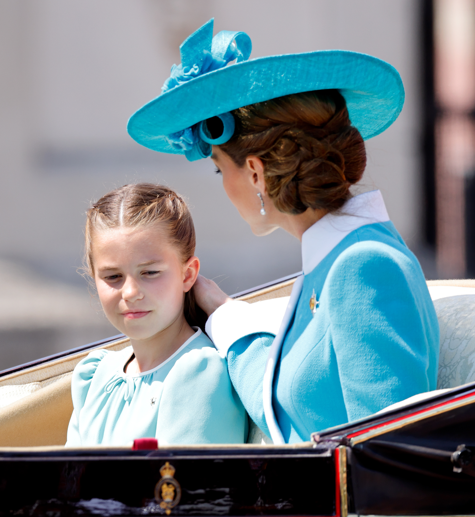 Princess Charlotte of Wales and Catherine, Princess of Wales return to Buckingham Palace. Catherine looks radiant in her aquamarine dress, wide-brimmed hat, and brunette locks styled in a soft updo while Charlotte glows in her white and aquamarine dress, voluminous brown hair, worn loose with a neat center part.