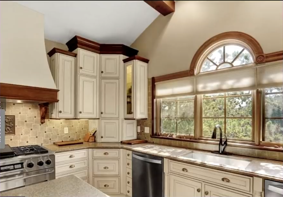 In the sixth photo, another view of the kitchen reveals a tiled backsplash, stainless-steel range and dishwasher beneath the countertops. A large window with an arched upper section overlooks the greenery outside.