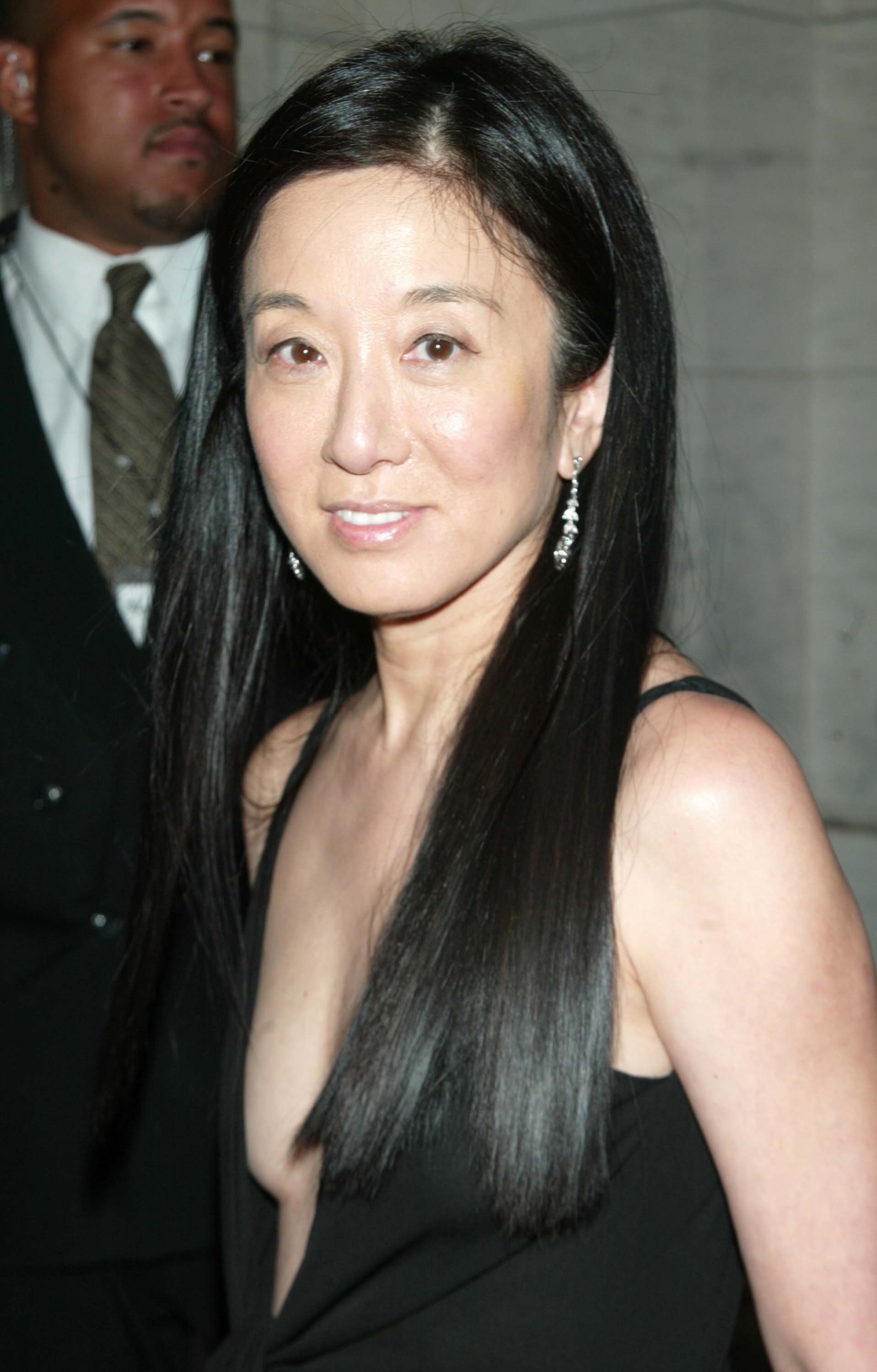 Vera Wang arrived at the New York Public Library for the 21st Annual CFDA Awards on June 3, 2002, in New York City, turning heads in a daring black gown featuring a plunging neckline. The designer complemented the striking look with dangling diamond earrings, a fresh, natural beauty palette, and her dark locks styled sleek and straight past her shoulders. | Source: Getty Images