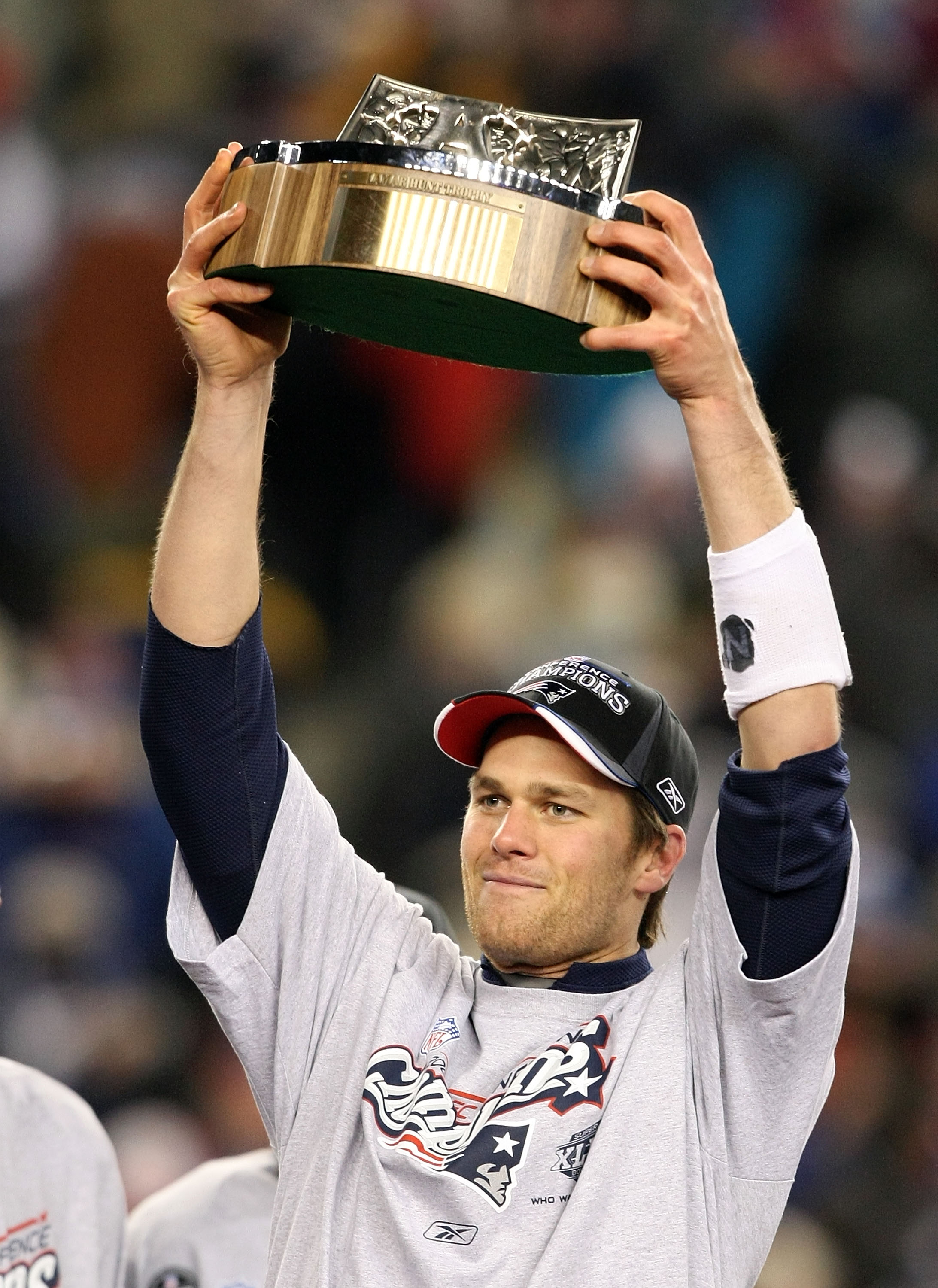 With a triumphant smile lighting up his face, Tom Brady #12 of the New England Patriots hoists the Lamar Hunt AFC Championship trophy high after a hard-fought 21–12 victory over the San Diego Chargers.