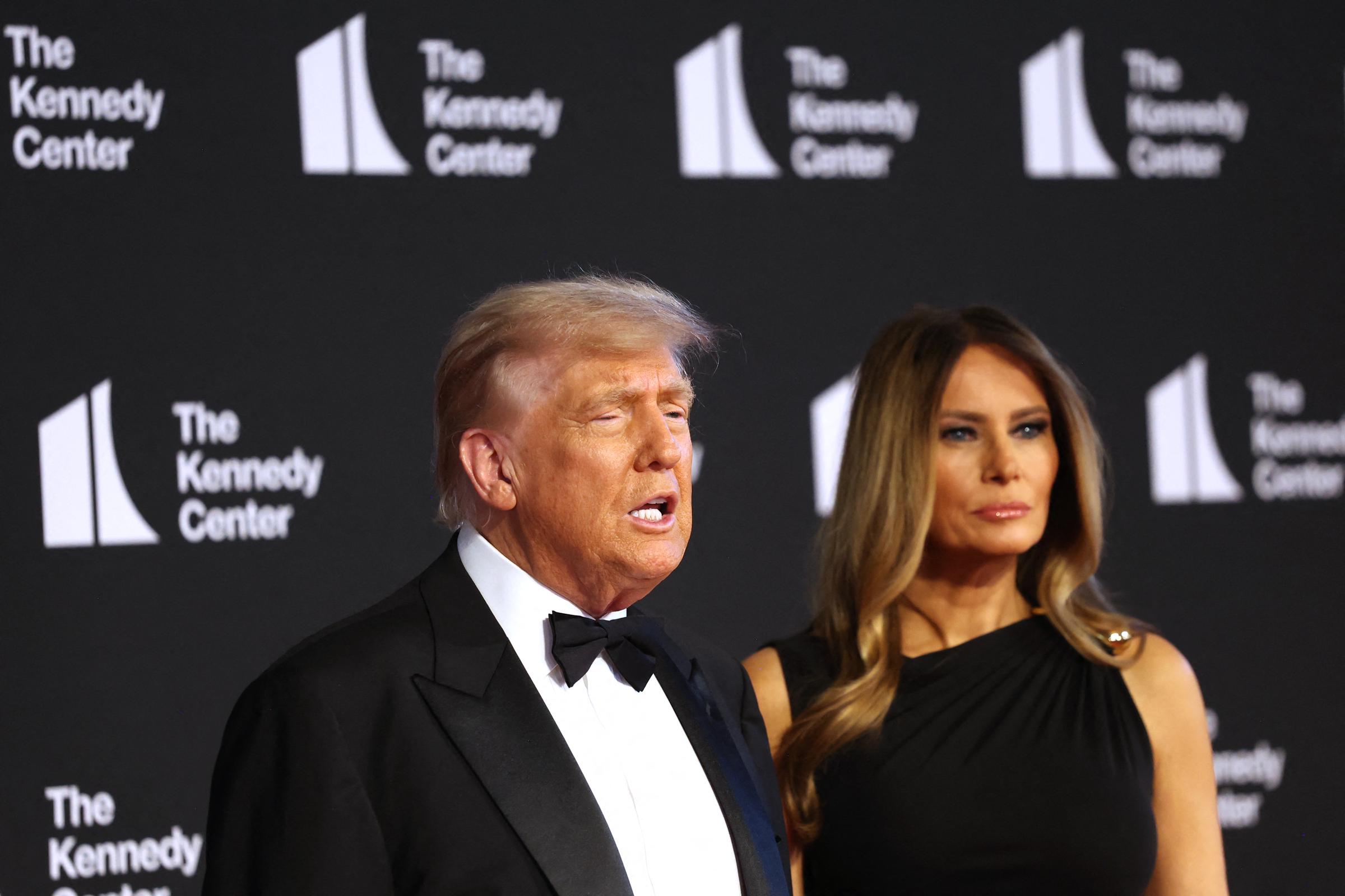 The president speaks to the press while the first lady looks ahead with a composed expression as the pair appear on the red carpet at the Kennedy Center's opening night event.