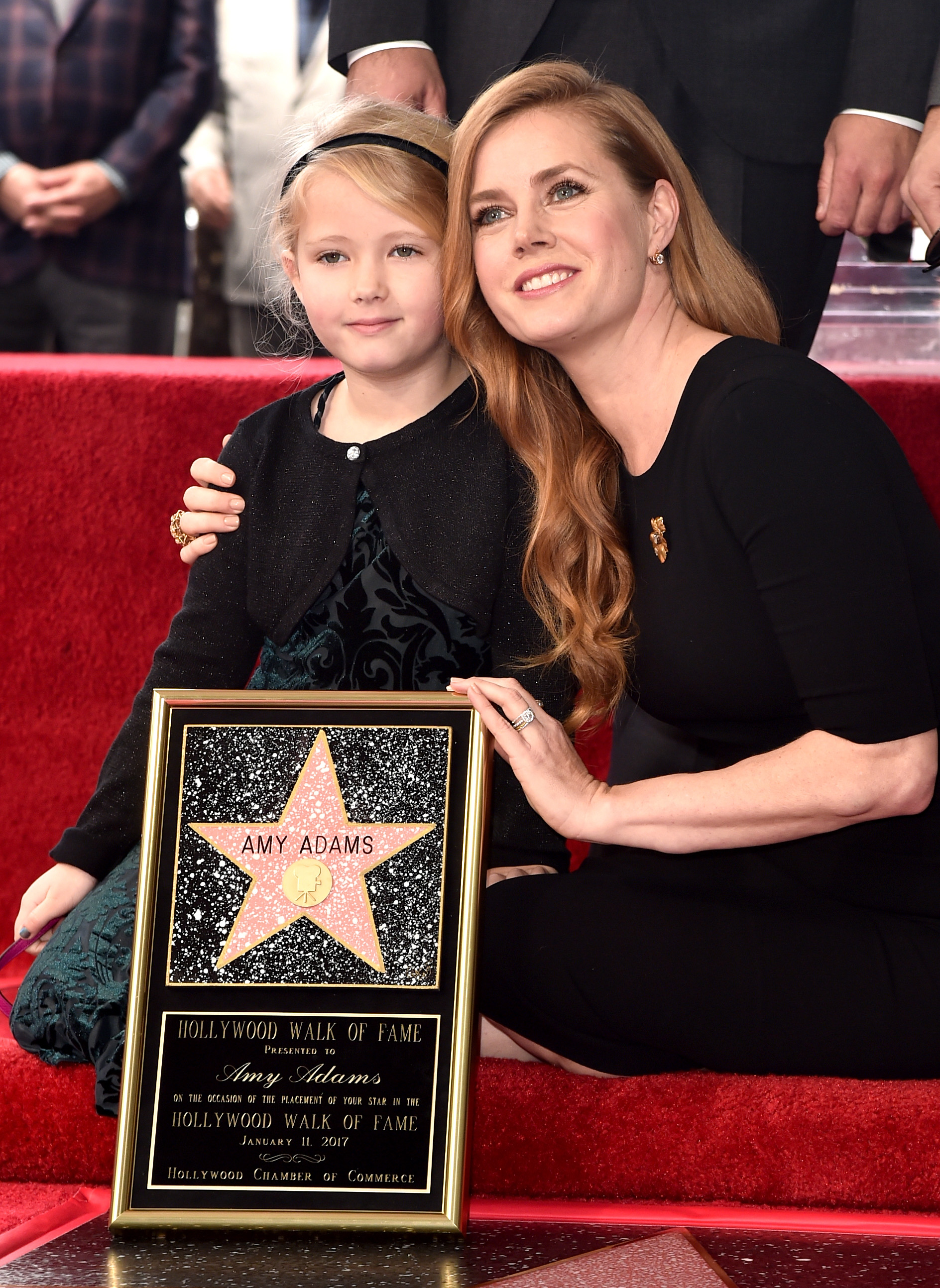 Amy Adams kneels beside Aviana Olea Le Gallo while posing with the plaque from Amy's Hollywood Walk of Fame ceremony. The mother and daughter smile together as Amy celebrates the milestone honor.