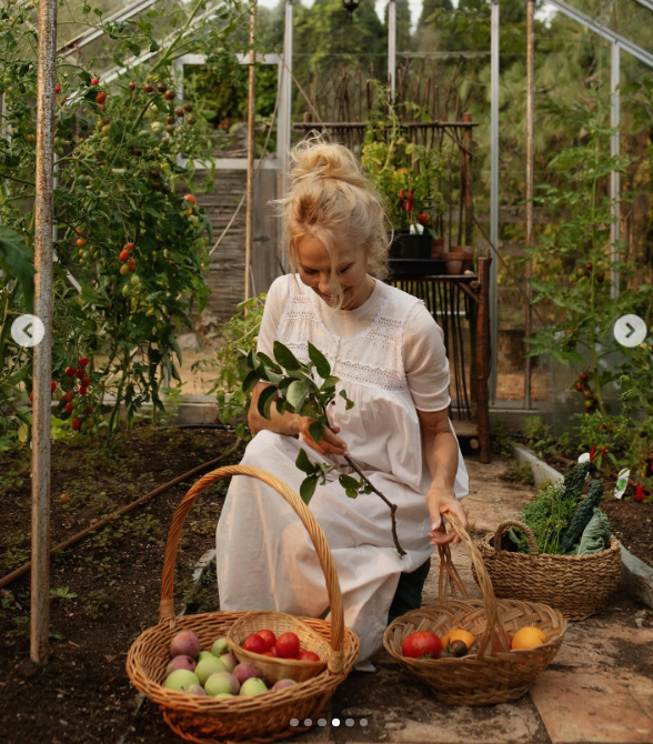 Inside a sunlit greenhouse at Arcady, Pamela Anderson kneels in a vintage white nightgown, cradling a freshly clipped branch alongside woven baskets laden with homegrown apples, heirloom tomatoes, and citrus. Highlighting the harvest for her show "Pamela's Cooking with Love," she celebrated bringing world-class chefs to Vancouver Island, calling the farm-based cooking project everything she could ever ask for. | Source: Instagram/pamelaanderson