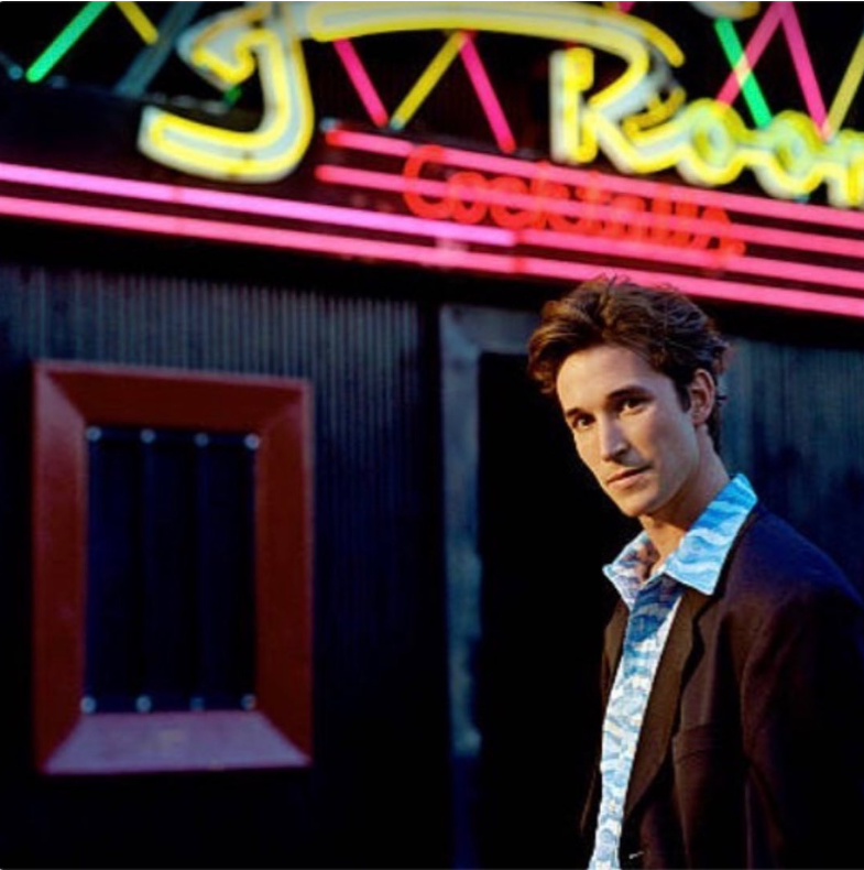 The actor as a young-adult poses outside a neon-lit venue in a vintage photograph from his earlier years in Hollywood, sporting a patterned shirt and dark blazer. | Source: Instagram/therealnoahwyle