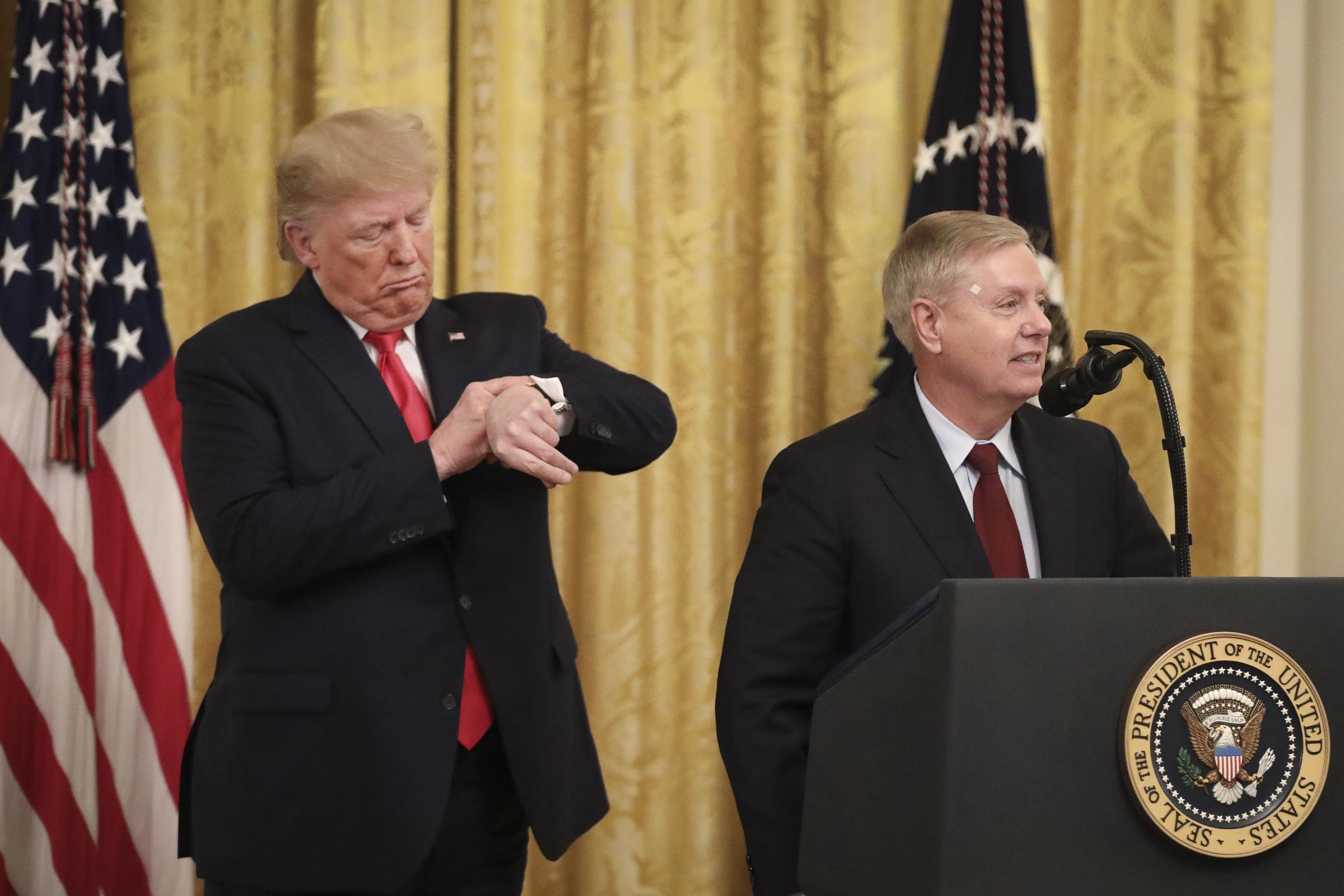 Standing beside President Donald Trump during a White House event, Lindsey Graham addresses judicial confirmations as Trump playfully checks his watch. The lighthearted exchange reflected the close political alliance the two developed after years of once-public disagreements. | Source: Getty Images
