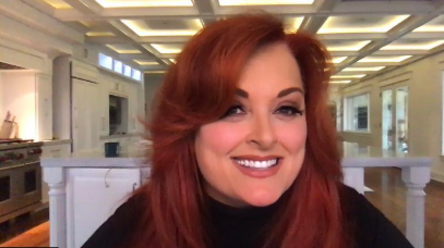 Wynonna smiles toward the camera with a large white kitchen visible behind her. The room's illuminated ceiling panels, cabinetry, and island provide a detailed view of the interior shown during her television appearance. | Source: Instagram/wynonnajudd