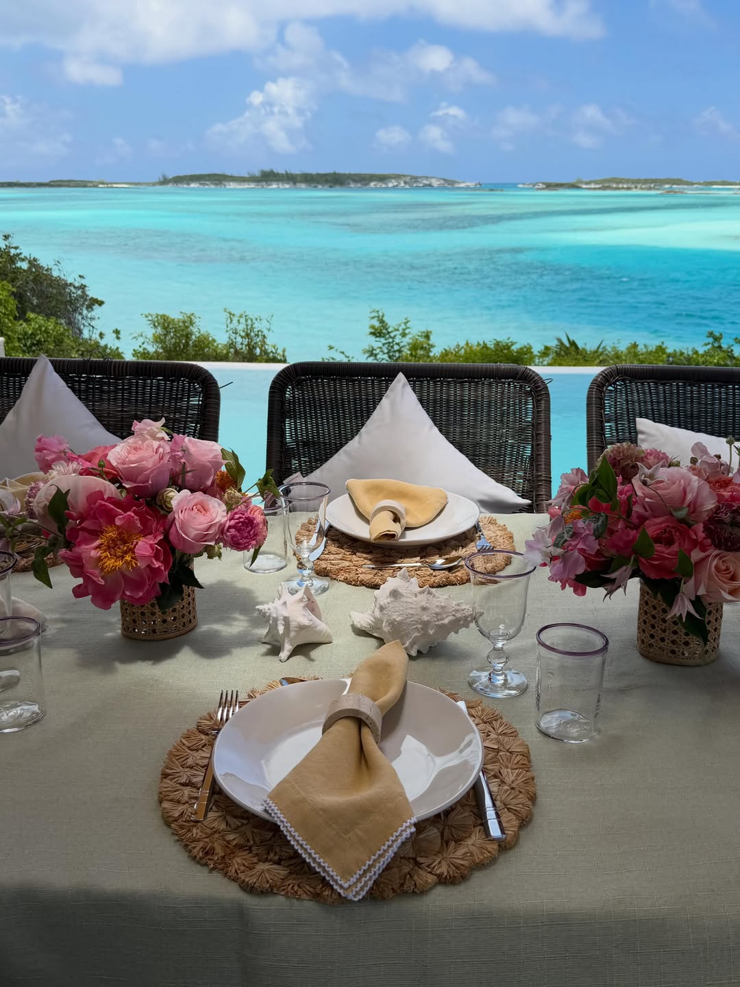 Pink floral arrangements and seashell accents decorate a seaside dining table, framed by panoramic views of the Bahamas' crystal-clear waters. | Source: Instagram/bettinatrump