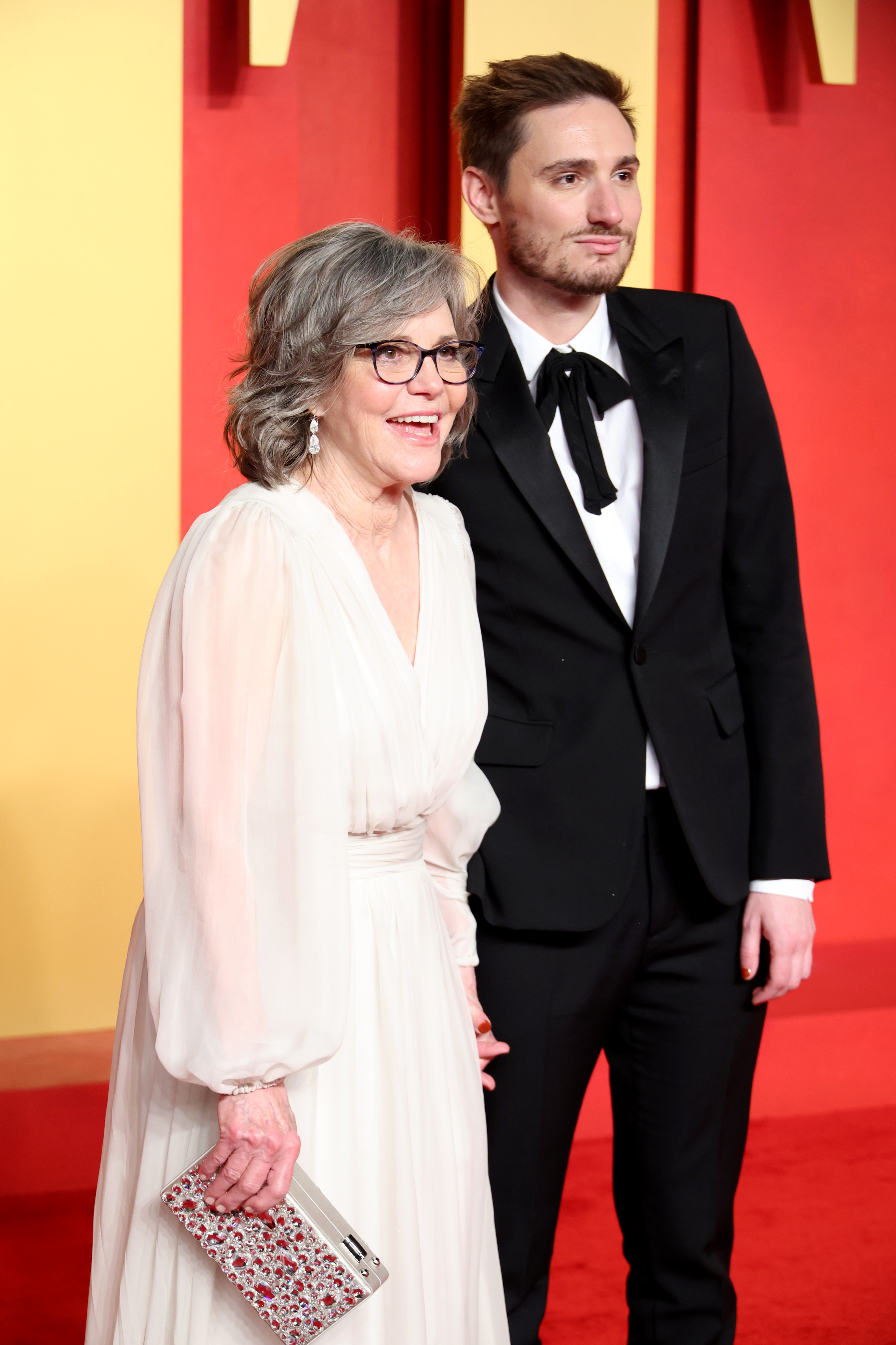At the same event, Sally Field poses with Samuel Greisman, wearing a gorgeous white dress paired with an elegant purse, completing her graceful look.