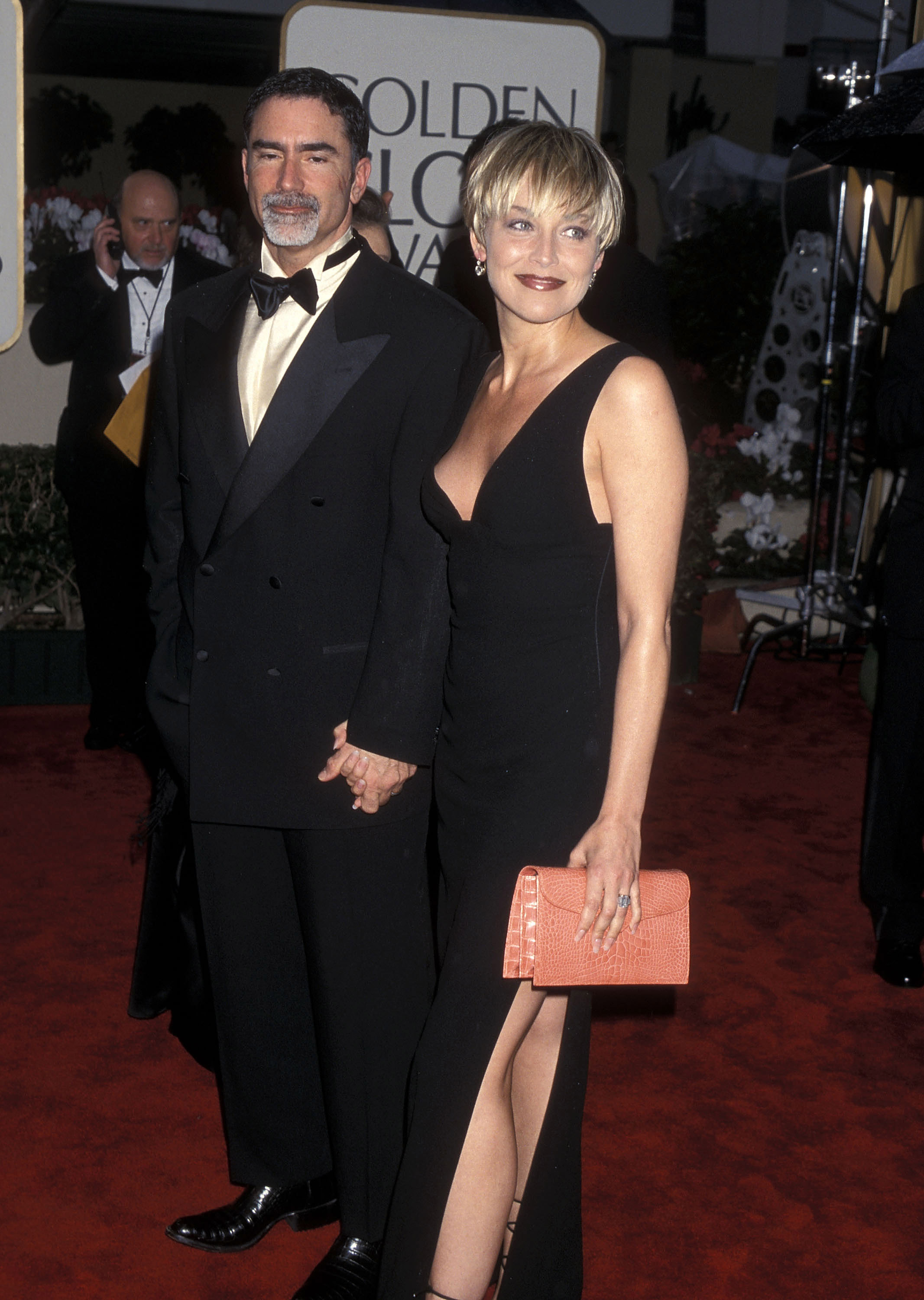 Sharon Stone and Phil Bronstein hold hands at the 57th Annual Golden Globe Awards on January 23. Stone wears a black gown with a thigh-high slit and carries a coral clutch.