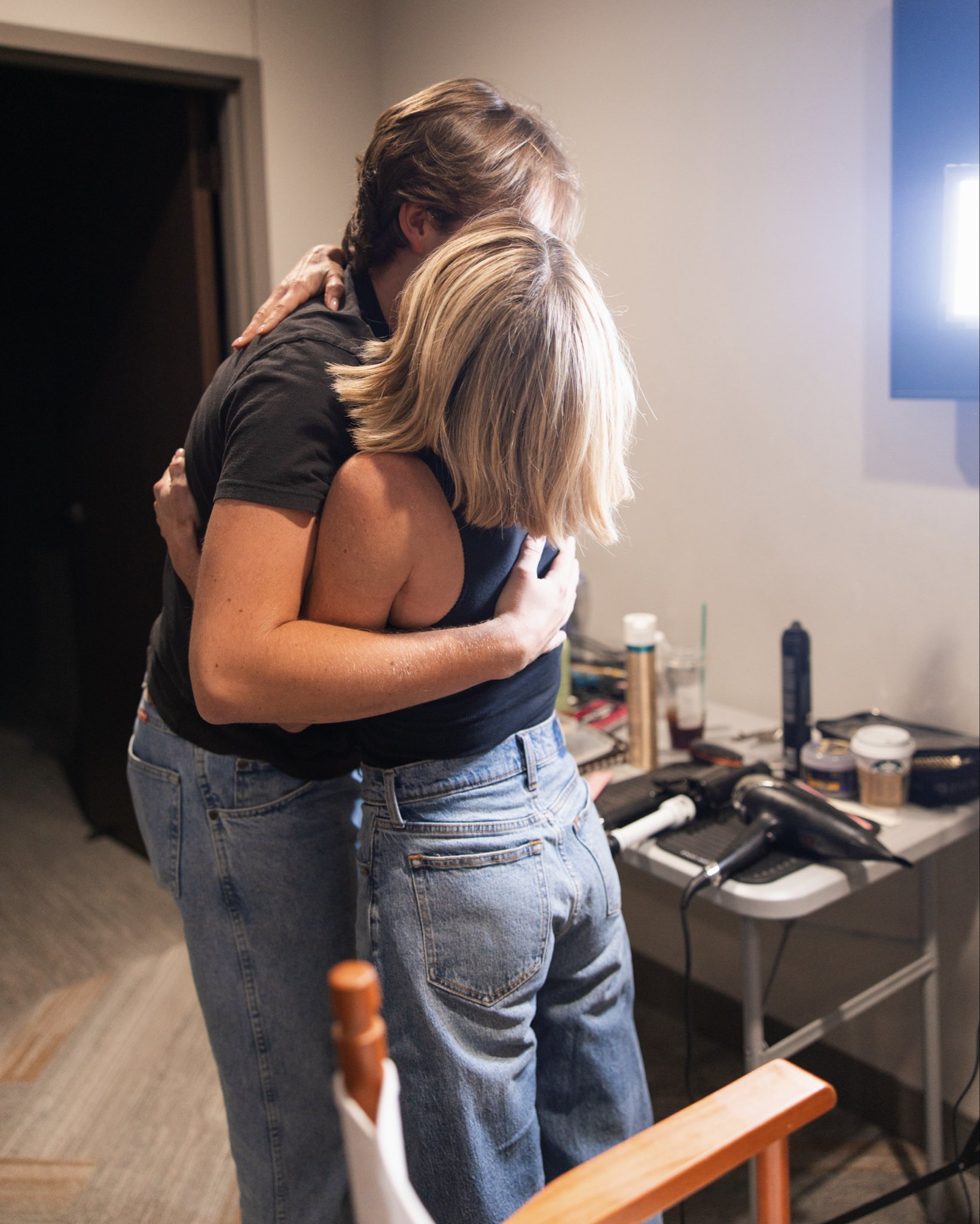 Candace Cameron Bure shares a tender backstage embrace with her son, Maksim Bure, resting her head on his shoulder in the dressing room while both wear coordinating black tops and light-wash blue jeans. | Source: X/candacecbure