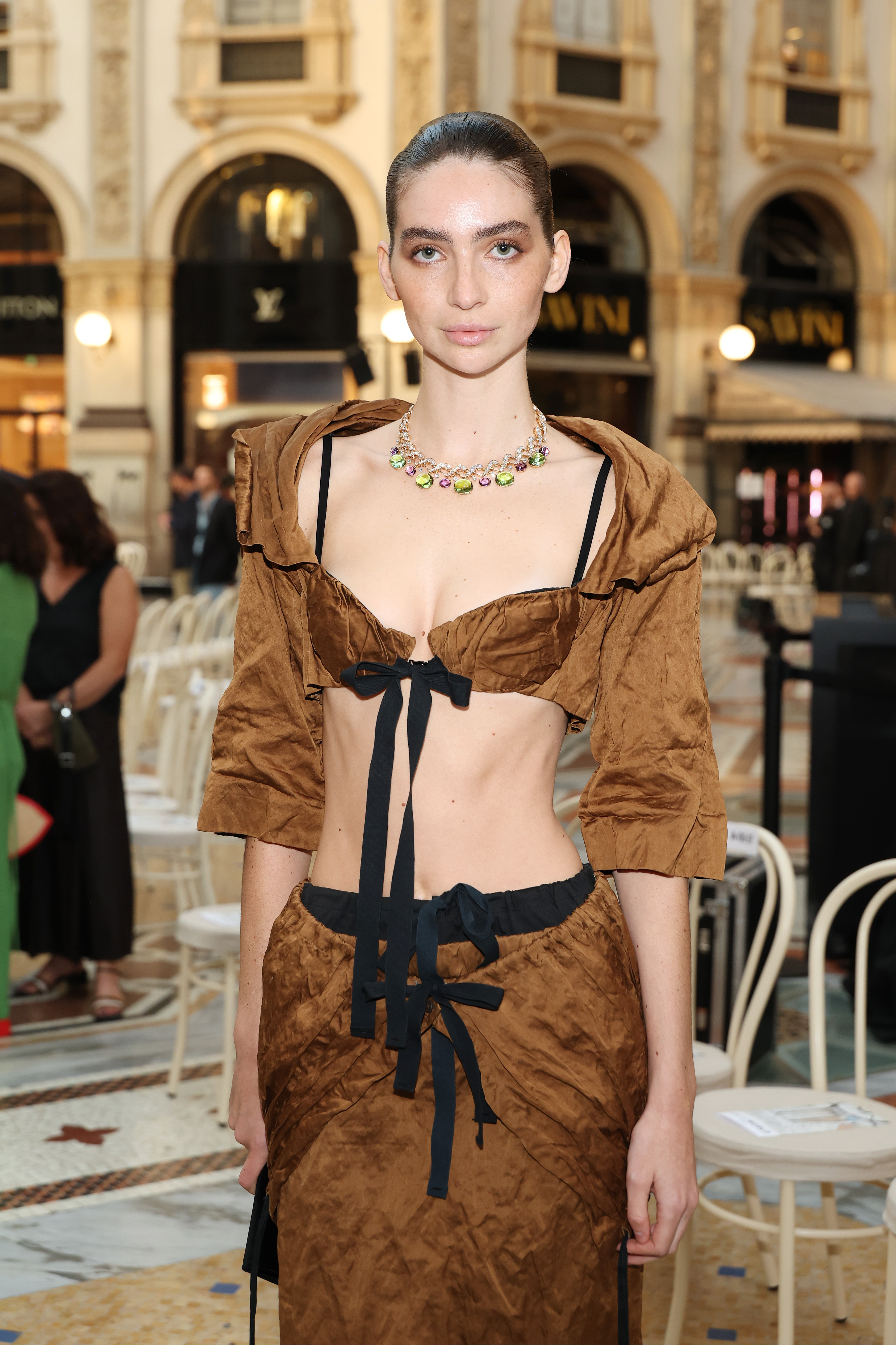 Walker poses for photographers inside the venue, with the tighter shot emphasizing her colorful jeweled necklace, plunging neckline, and black bow. | Source: Getty Images