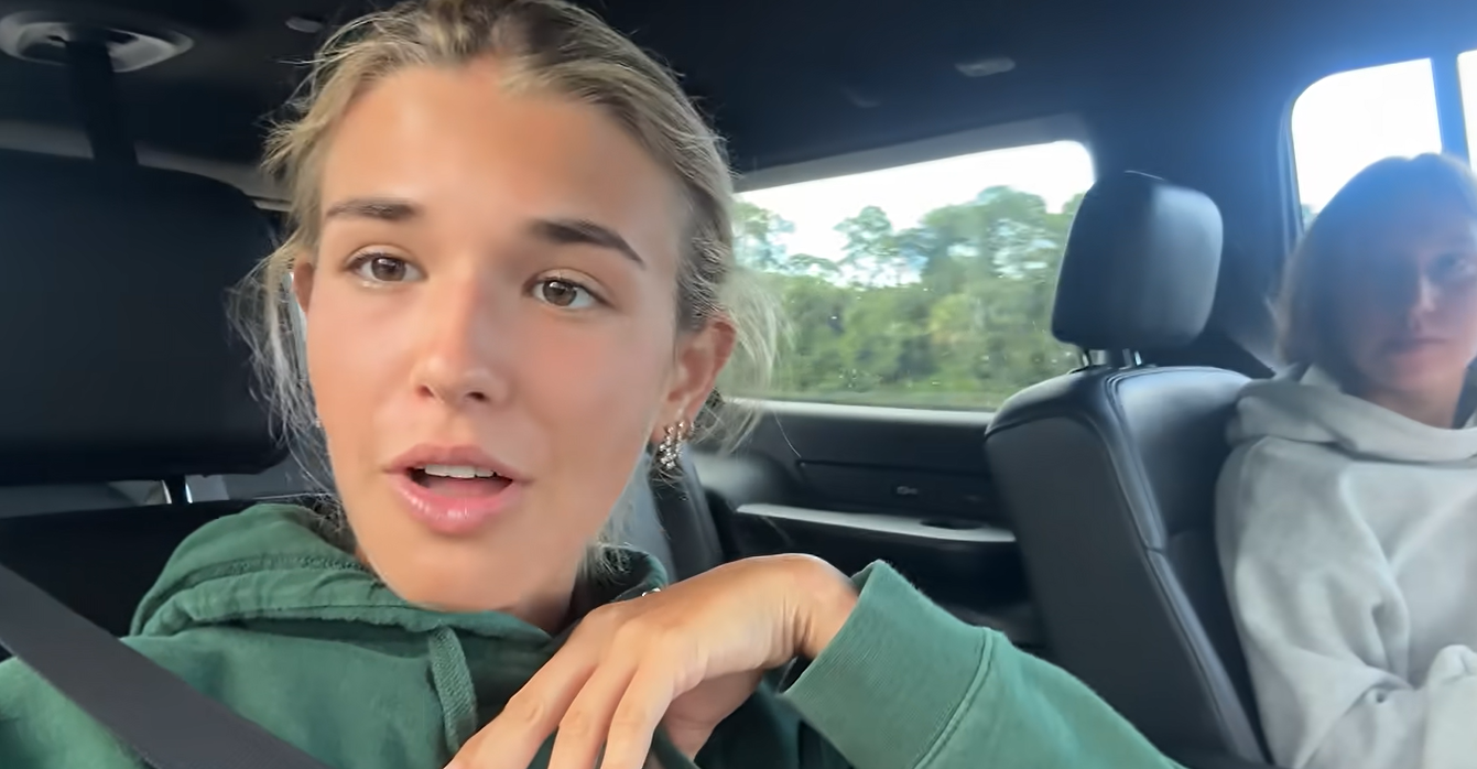 Kai Trump speaks to the camera from a car while wearing a green hoodie. She revealed that she had contracted strep throat during her first week of school and returned to Jupiter, Florida, to recover with help from her mother. | Source: Youtube/kaitrump
