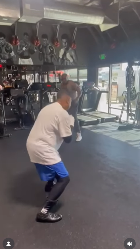 Martin Lawrence dips into a lower stance mid-drill, continuing his shadowboxing sequence as the training partner follows along, both framed by gym machines and large front windows. | Source: Instagram/martinlawrence