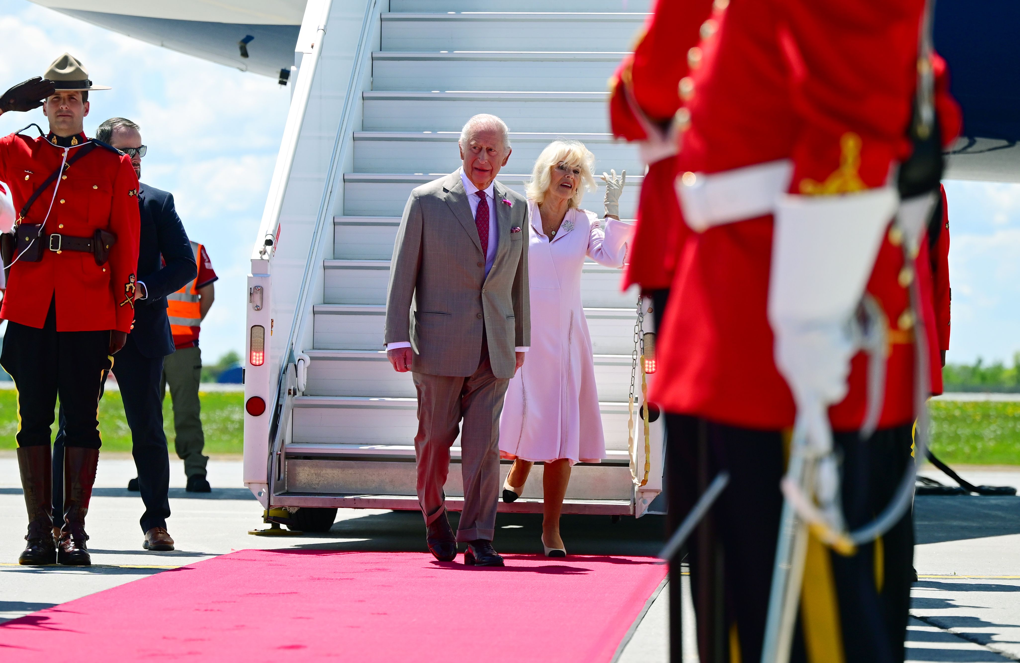 At the bottom of the stairs, King Charles III and Queen Camilla walk toward members of the Royal Canadian Mounted Police and the Canadian Armed Forces, who are lined up to welcome them.