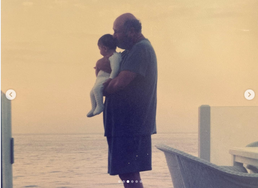 A softly lit, vintage-toned photo shows Rob Reiner standing near a body of water, cradling baby Romy in his arms, from a post dated March 6, 2022. | Source: Instagram/romyreiner