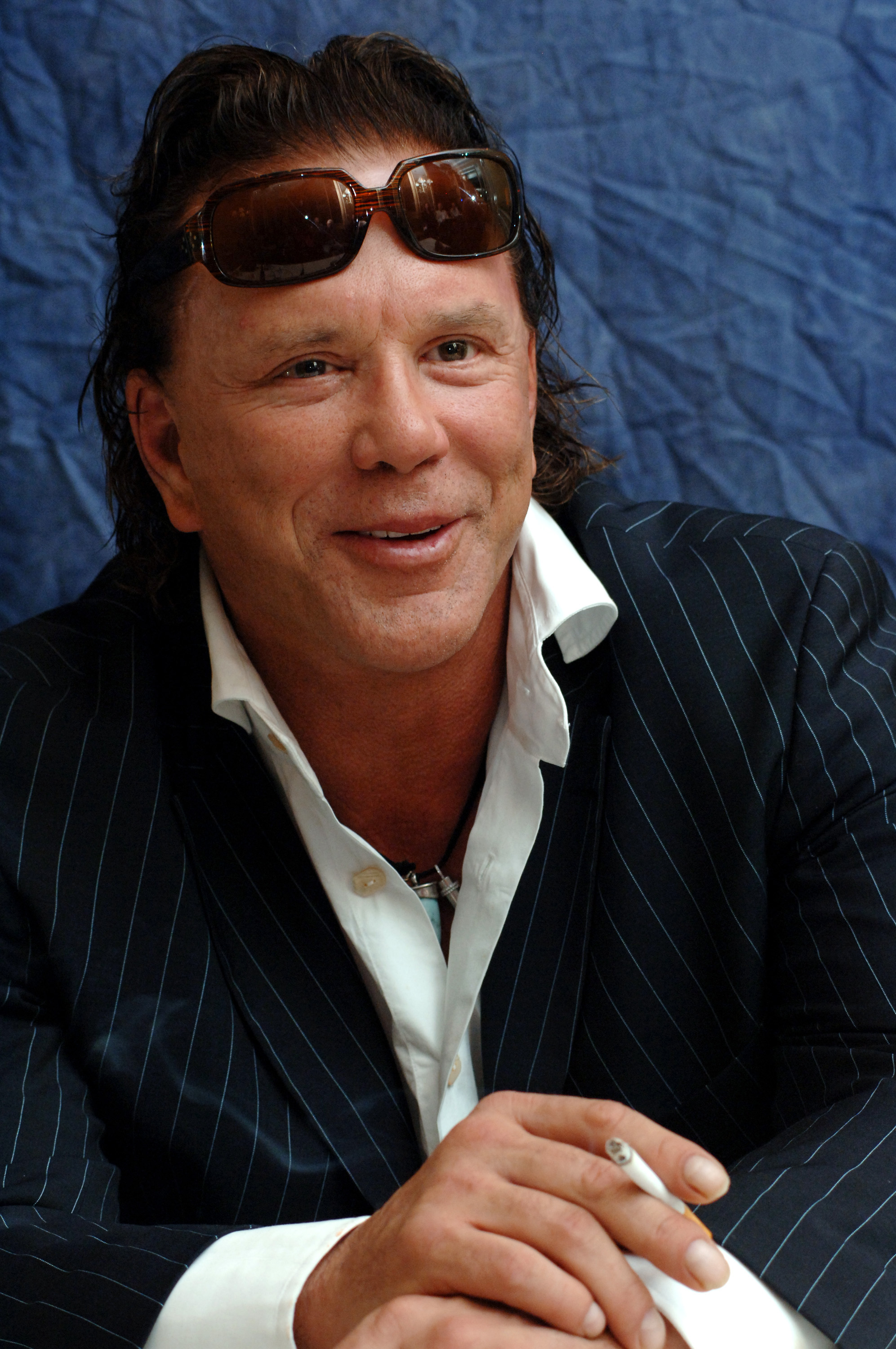 Mickey Rourke attends the "Domino" press conference at the Four Seasons Hotel in Beverly Hills, exuding rugged charm in a pinstripe suit and open-collar shirt. With sunglasses perched on his head and a cigarette in hand, he flashes a knowing smile that captures his rebellious charisma.