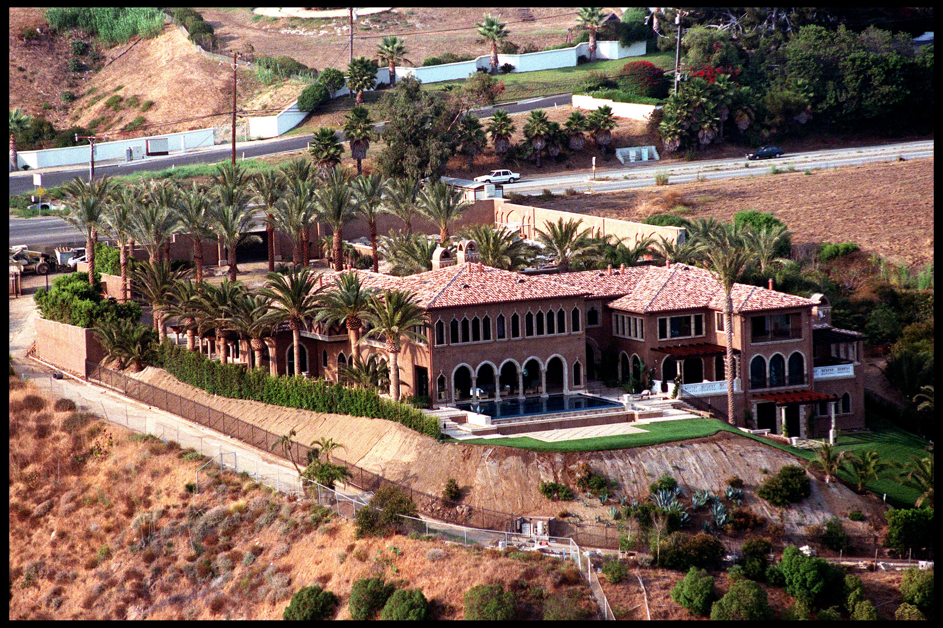 An aerial photograph captured pop icon Cher's newly built luxury estate overlooking the Pacific Ocean in Malibu, California, on July 29, 2000. The expansive Mediterranean-style residence features clay-tile roofs, multiple arched loggias, an infinity pool bordered by a manicured lawn, and surrounding grounds planted with mature palm trees set along the coastal hillside. | Source: Getty Images