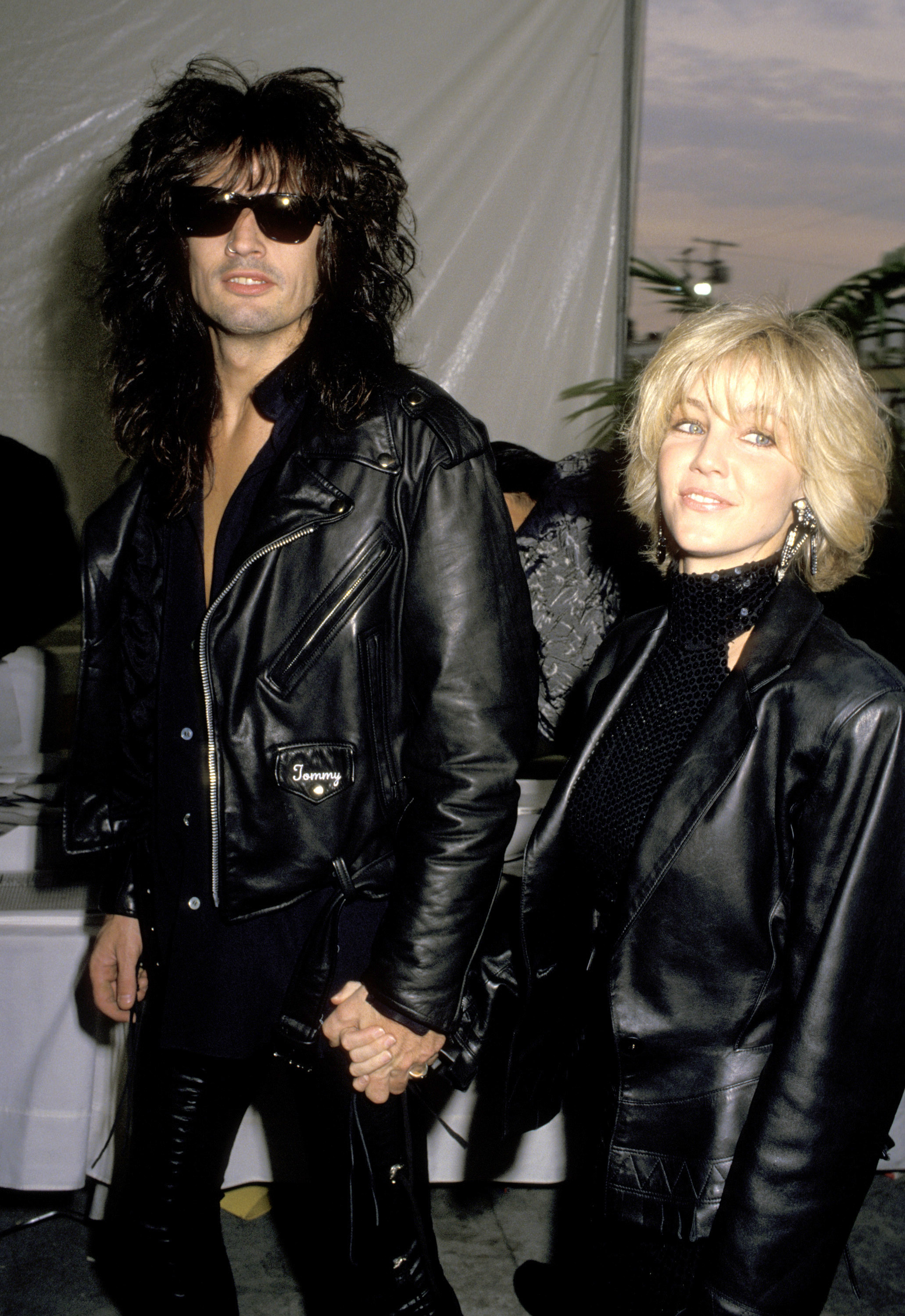 Heather Locklear and then-husband Tommy Lee make a bold entrance hand-in-hand at the 32nd Annual Grammy Awards on February 21, 1990. The rock-and-roll power couple matches in head-to-toe black leather, with Lee in dark sunglasses and an embroidered biker jacket, while Locklear debuts a textured blonde bob, drop earrings, and a sequined high-neck top beneath an oversized leather blazer. | Source: Getty Images