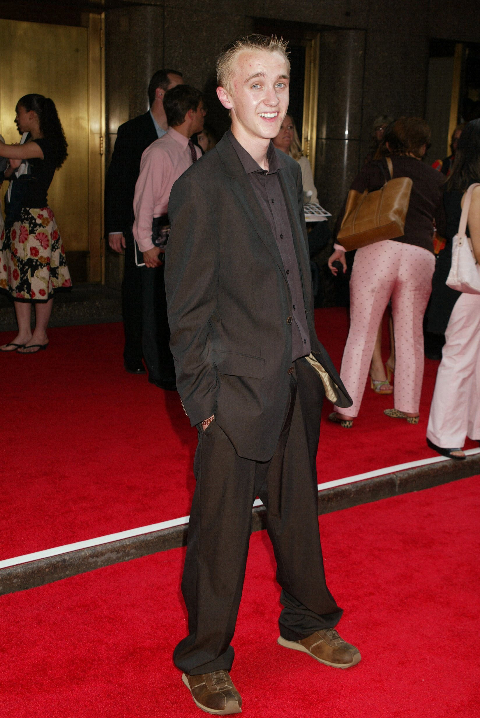 Tom Felton steps onto the red carpet with an easy grin, dressed in a relaxed suit that mirrors his youthful charm. The excitement of the "Harry Potter and the Prisoner of Azkaban" premiere buzzes around him as fans gather in anticipation. Confident and carefree, he stands as a young star enjoying every moment of the magic.